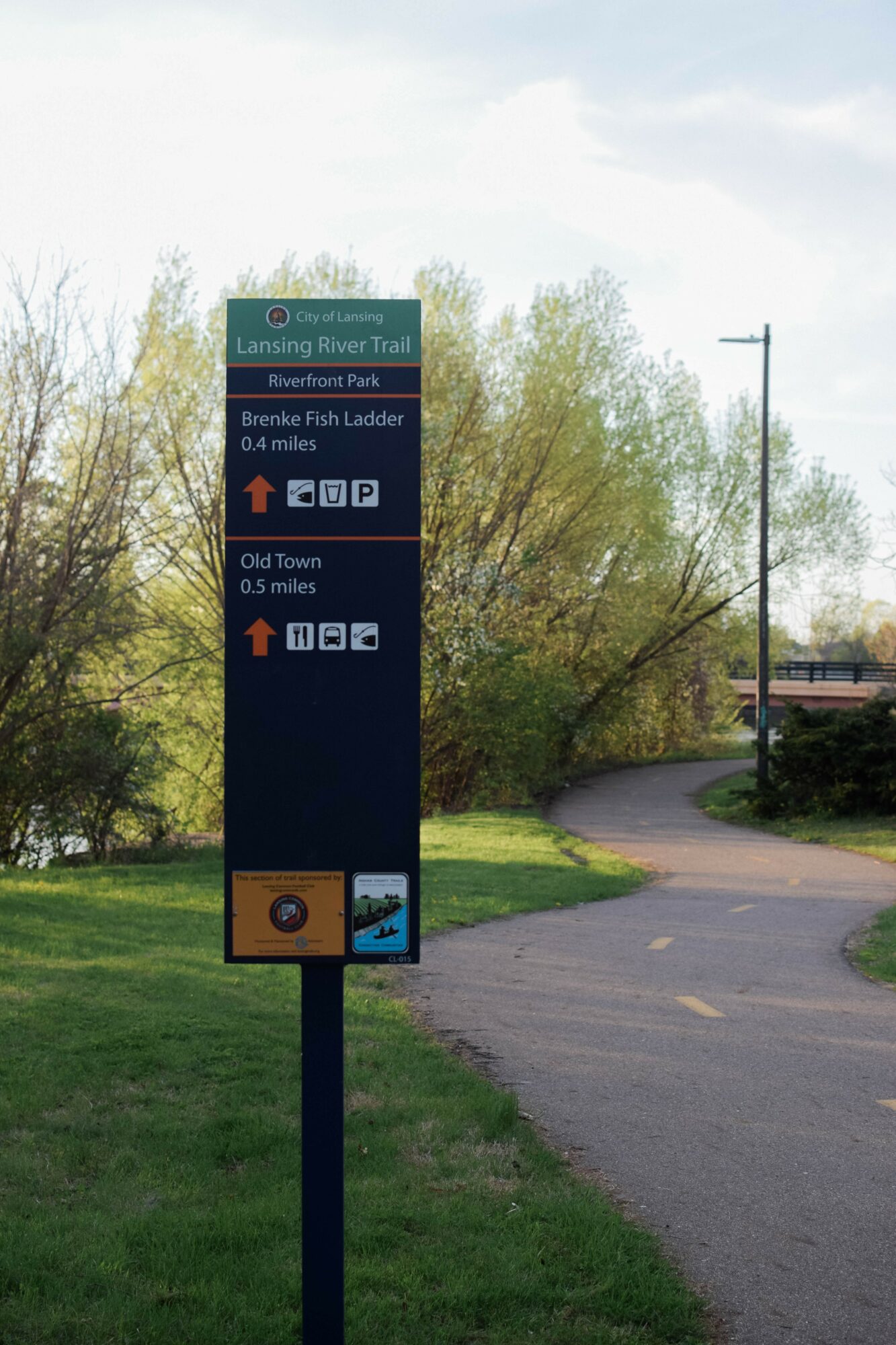Signpost with directions to Lansing River Trail and Brene Fikes Ladder, near a walking path and trees, daytime.