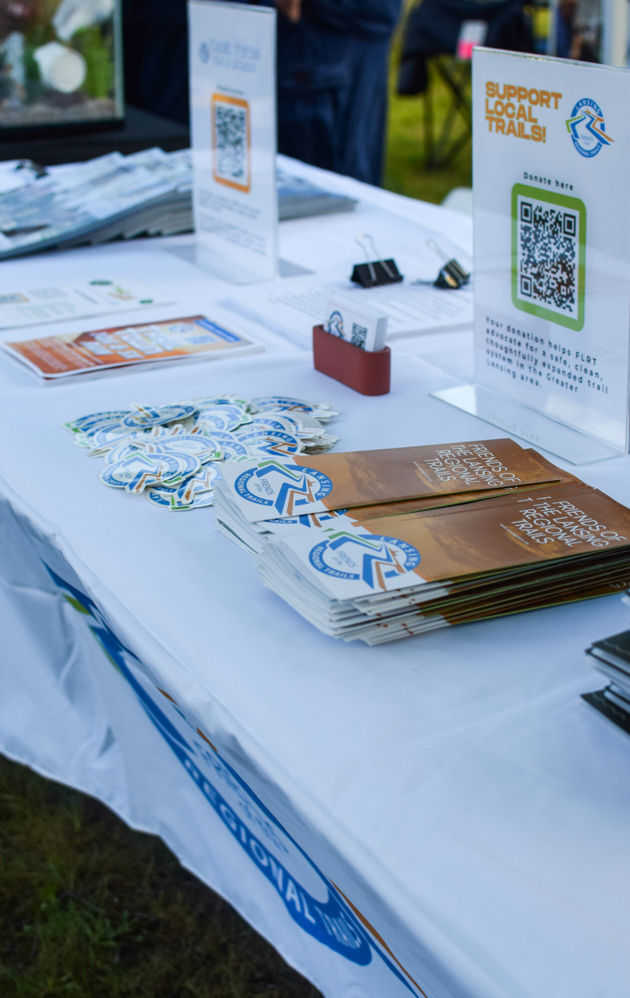Table with brochures, QR code sign, and promotional materials at an outdoor event.