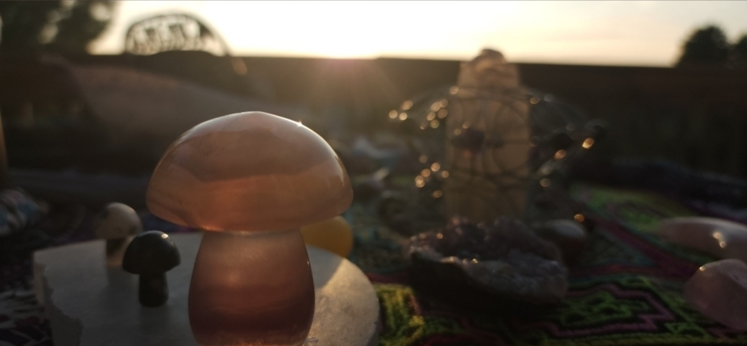 A mushroom-shaped object on a surface with other small objects and a background of a sunset sky.