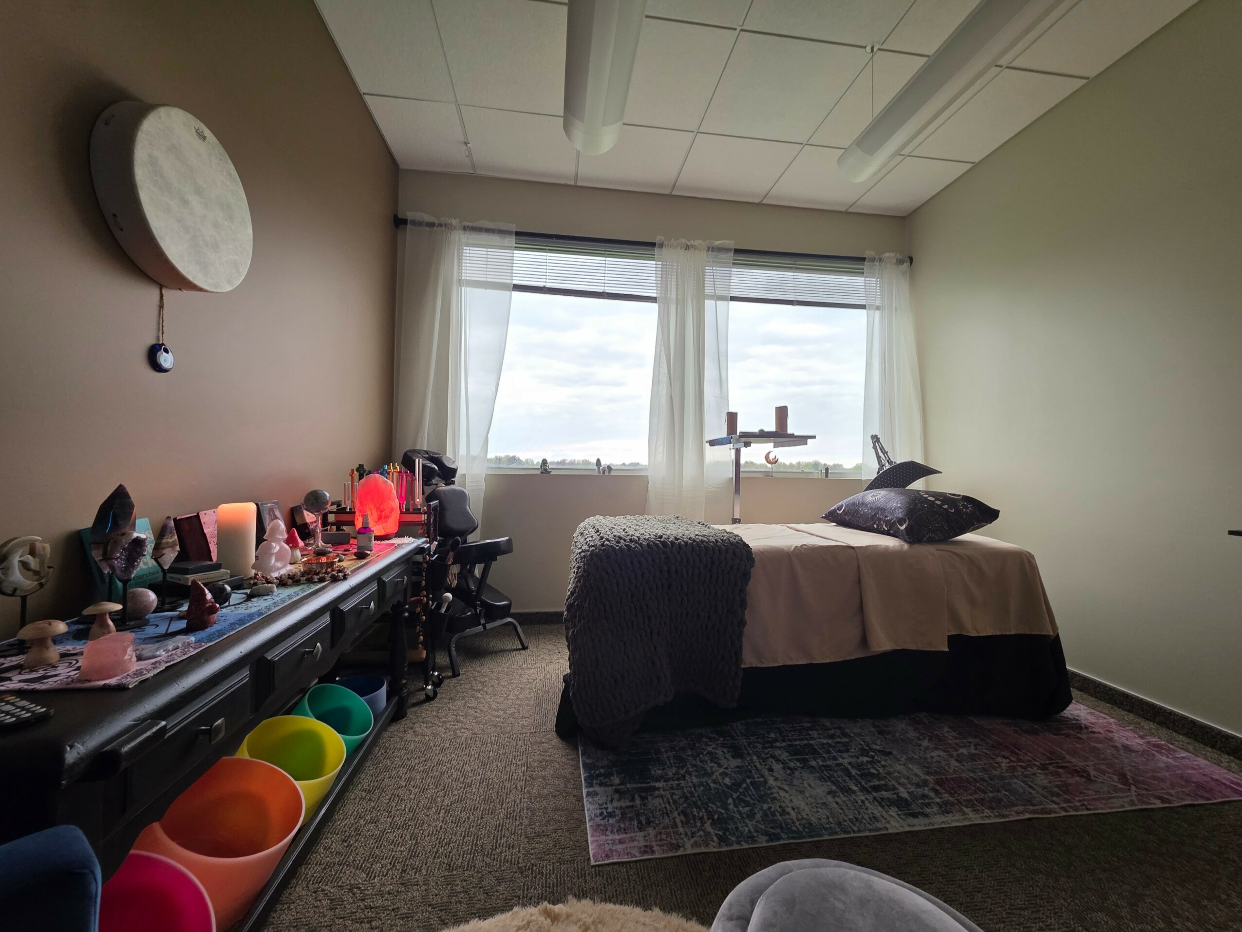 Room with bed, window, and various objects on a desk, including lamps and decorations, with a rug on the floor.