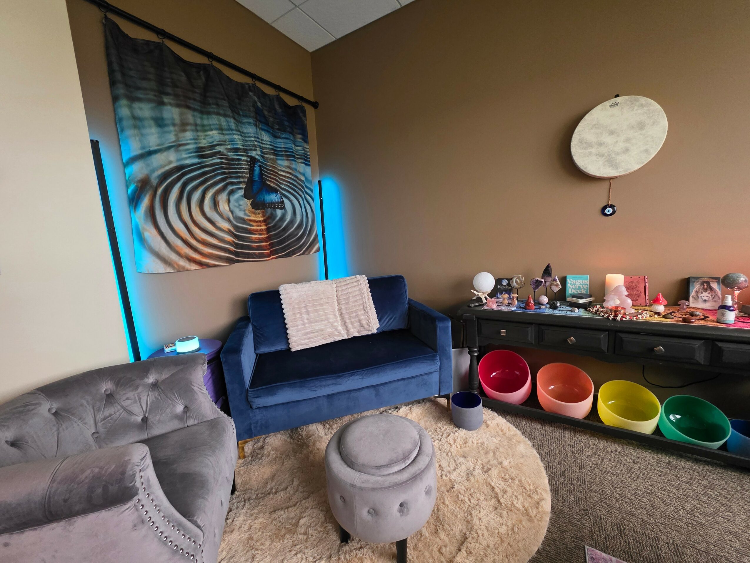 Room with a blue sofa, colorful bowls on a black table, and a circular wall decoration, viewed from the side.