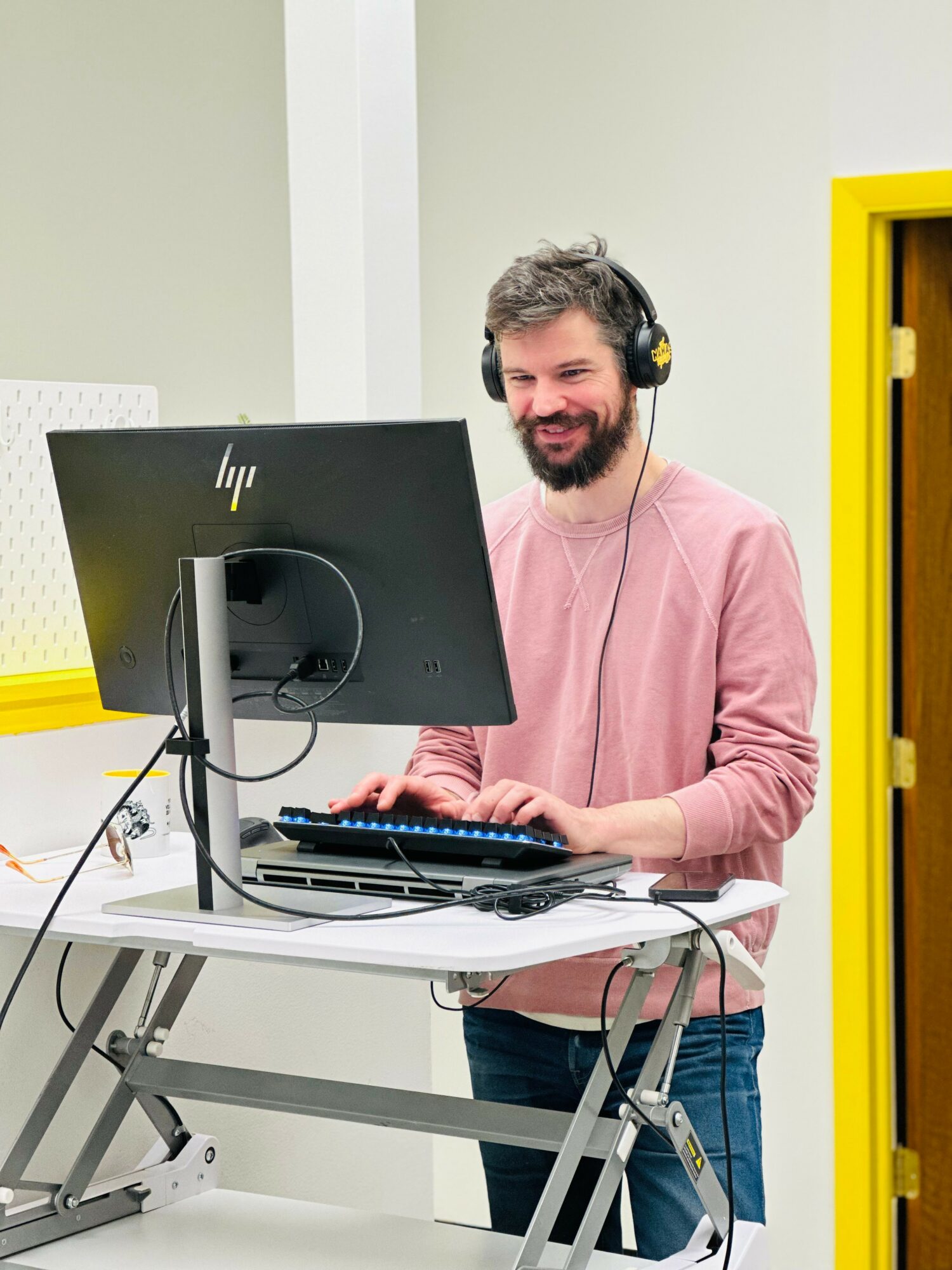 Man with headphones smiling at computer in a bright room with yellow accents.