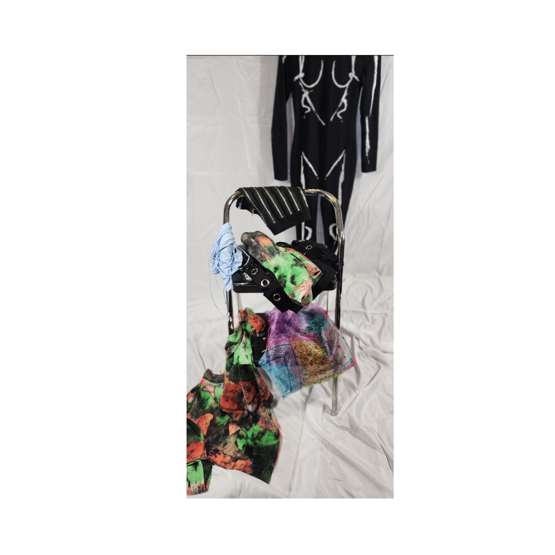 Clothes and bags arranged on a chair and floor, with a black dress hanging in the background.