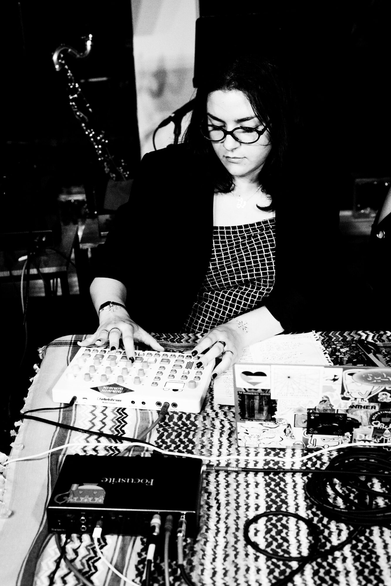 Woman with glasses looking at patterned fabric on table, surrounded by various items, in black and white.