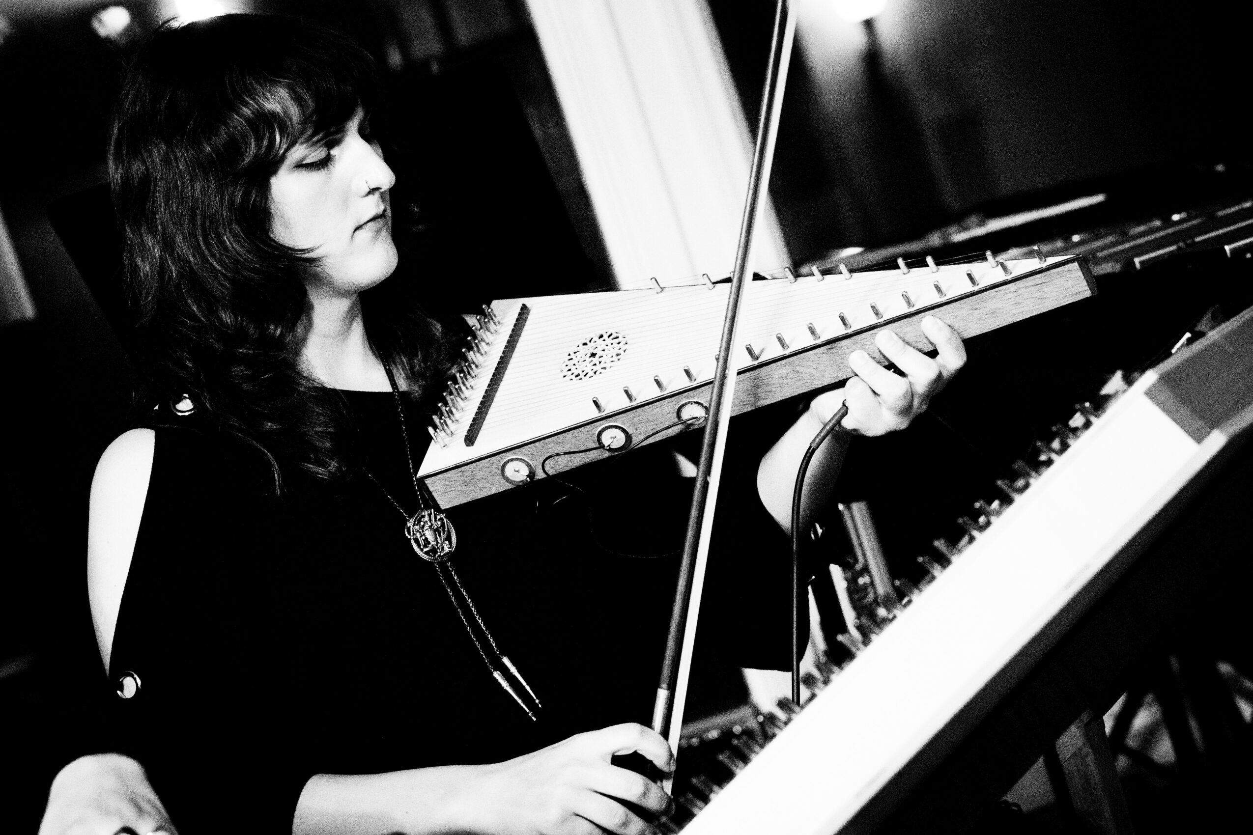 Woman playing a keyboard with a theremin, holding a bow, in a music studio, black and white image.