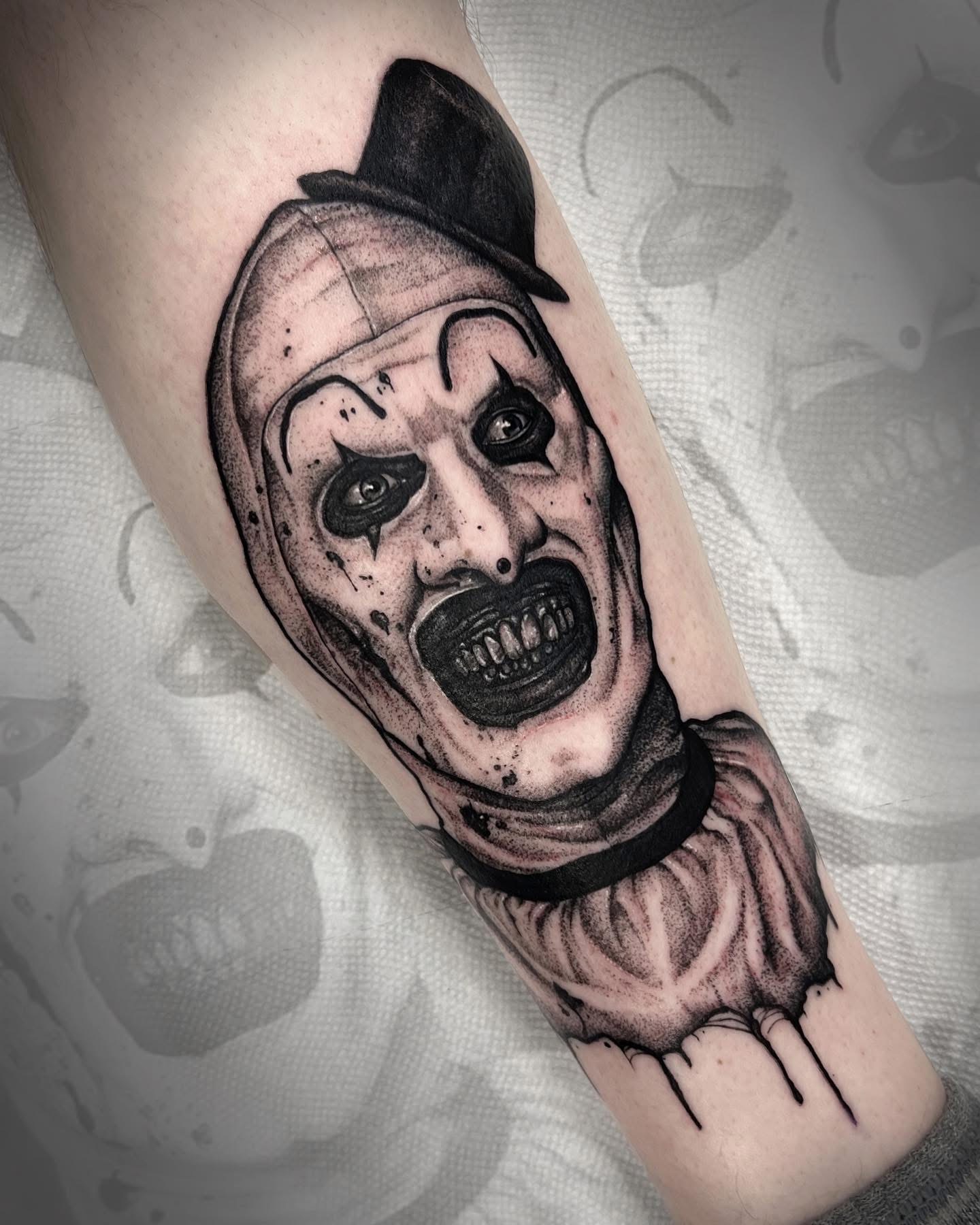 Tattoo of a clown with a hat, exaggerated facial features, and a distressed expression on the arm.
