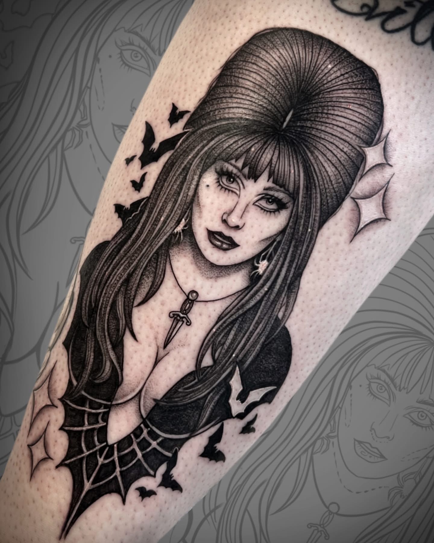 Black and gray tattoo of a woman with long hair, gothic makeup, surrounded by bats and a spider web, on skin.