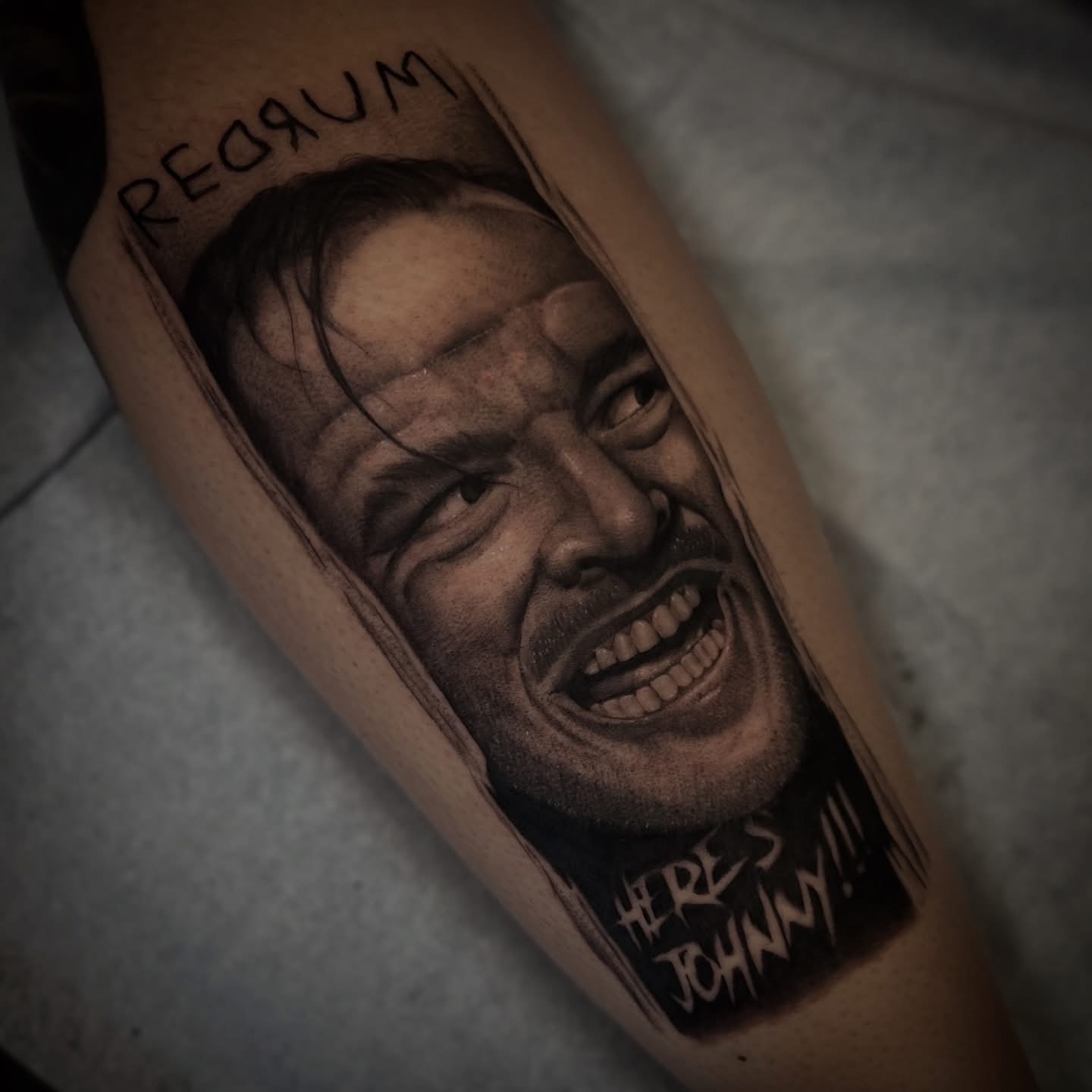 Tattoo of a smiling man's face with text above and below, on a person's arm.