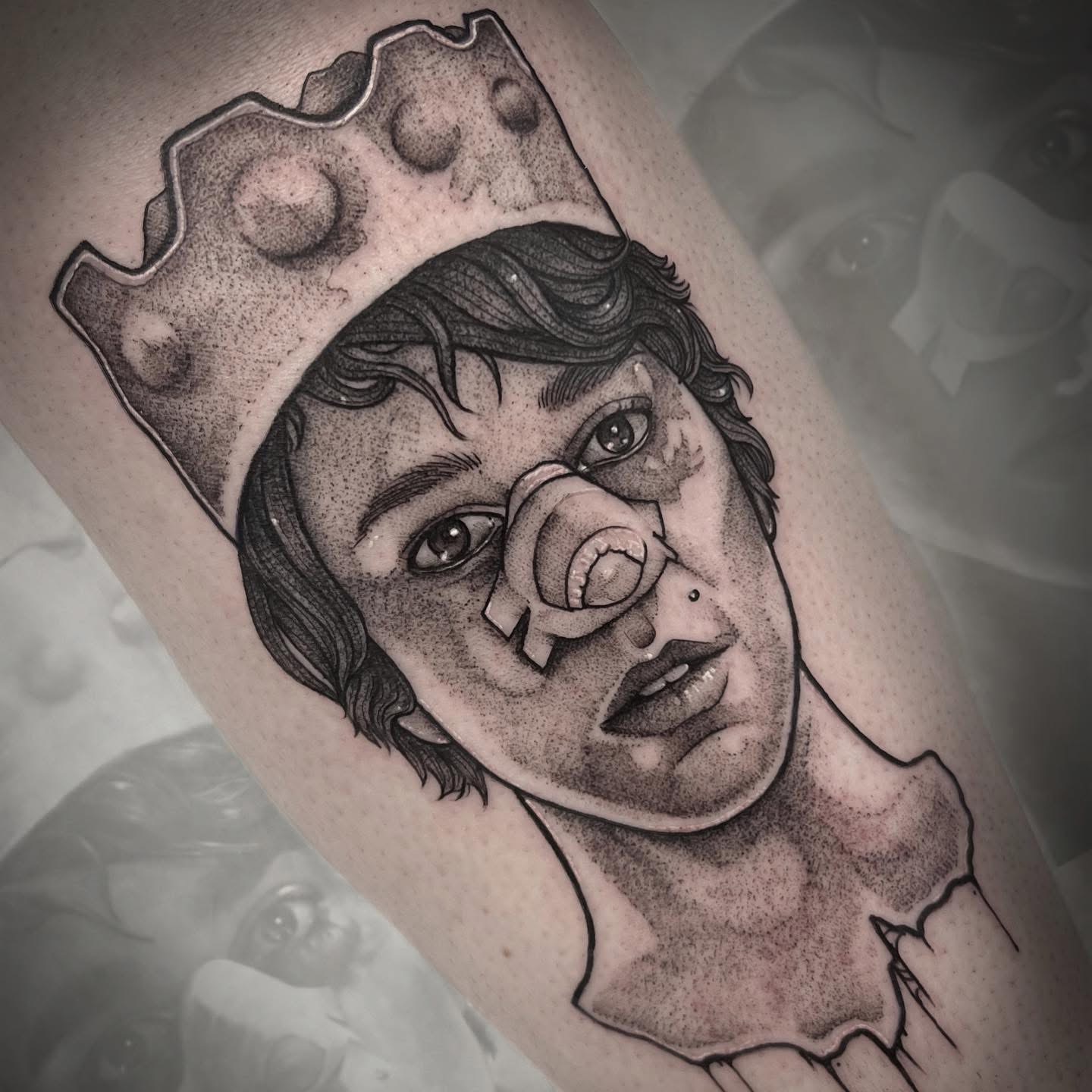 Black and gray tattoo of a woman with a crown and a nose bandage, detailed shading, on skin.