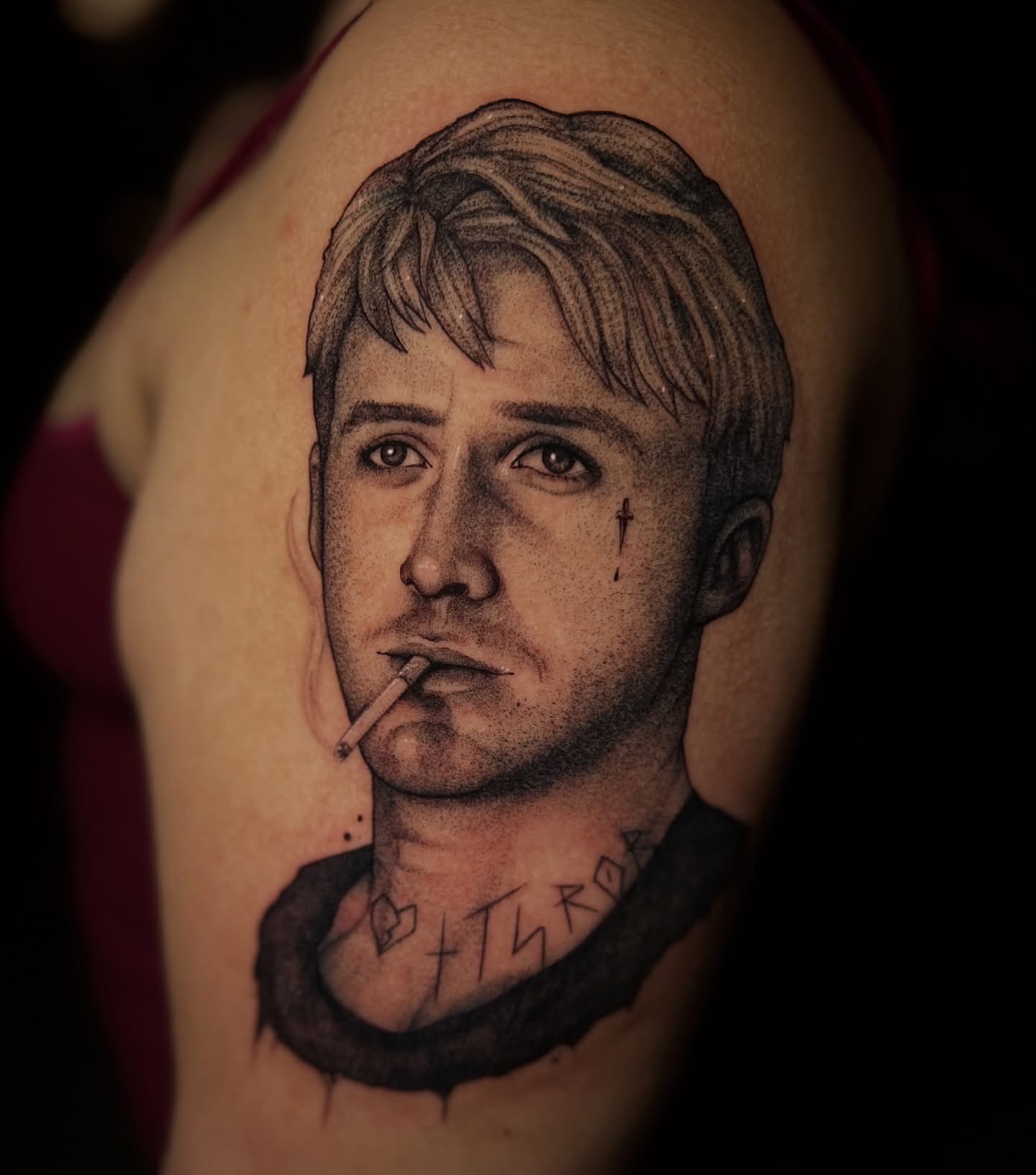 Tattoo of a young man with short hair, holding a cigarette, with a small cross near his eye and a necklace with symbols.