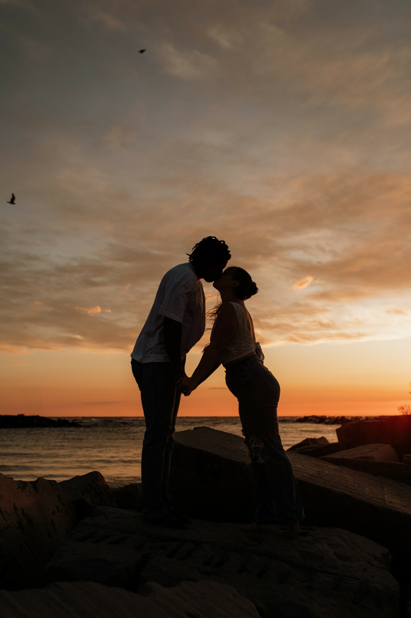 Silhouette of a couple holding hands on a beach at sunset, with a colorful sky and water in the background.
