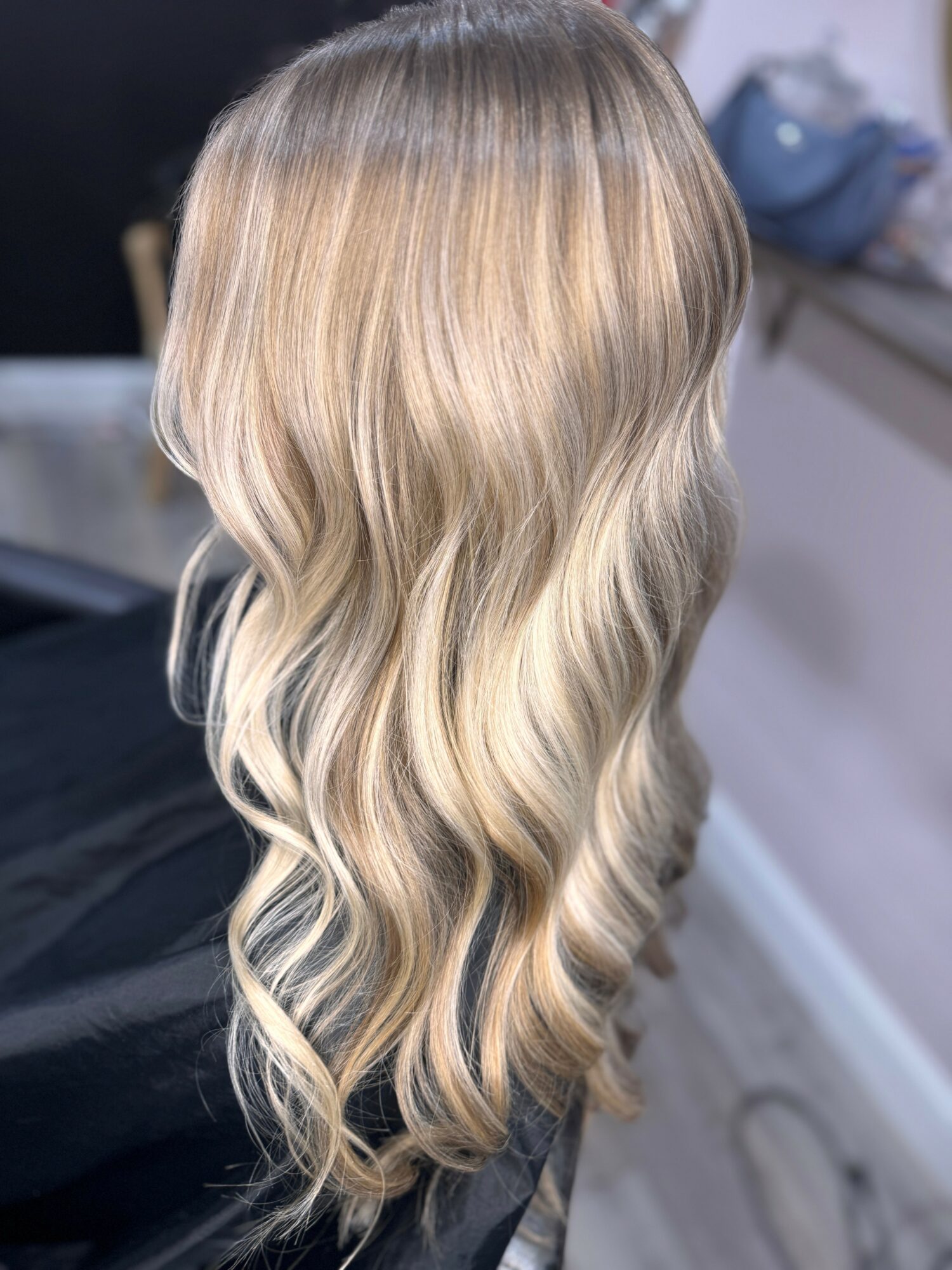 Long wavy blonde hair with darker roots, styled in loose waves, viewed from the back.