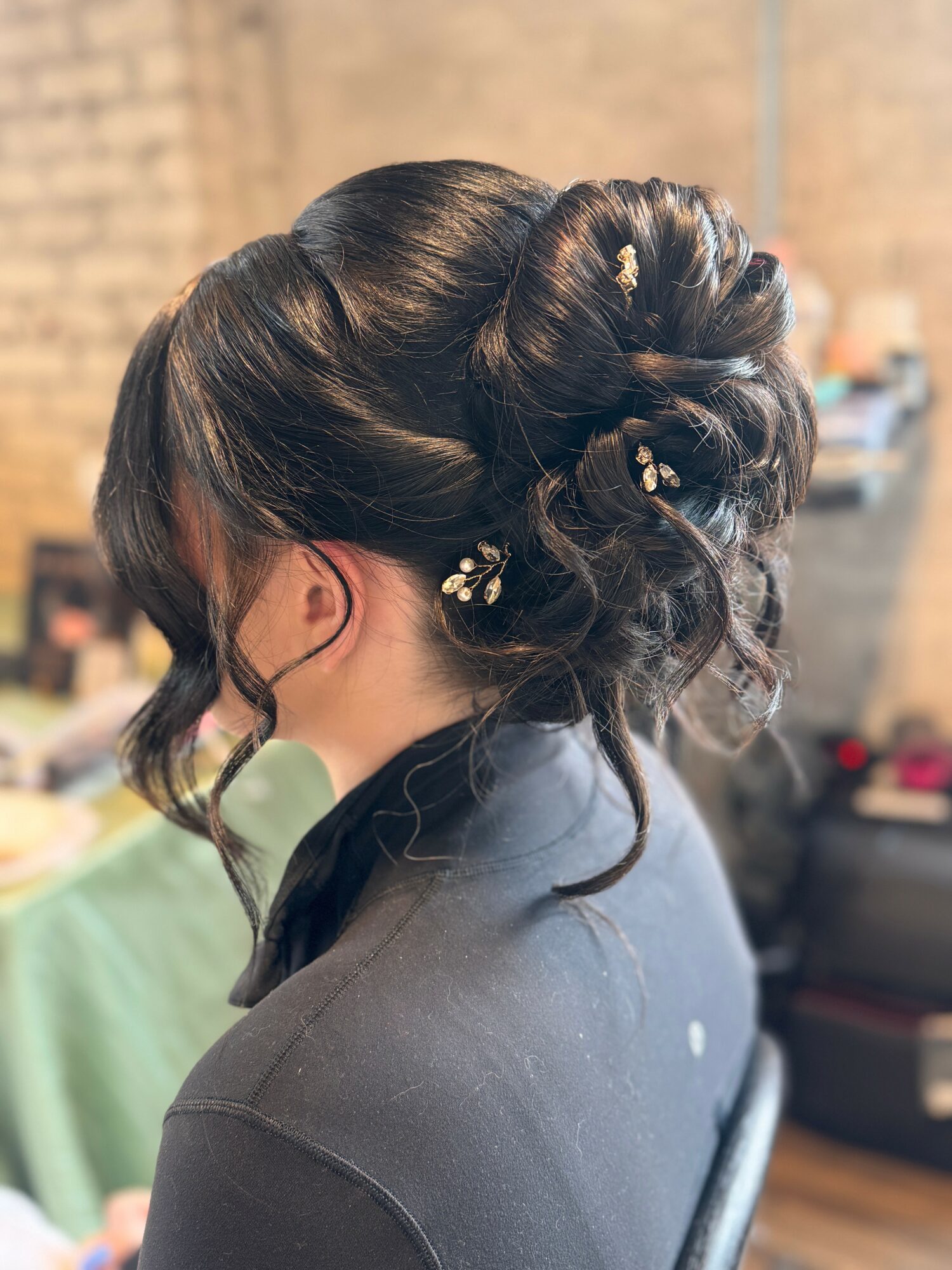 Side view of a woman with an elegant updo hairstyle decorated with small white flowers, wearing a dark top.