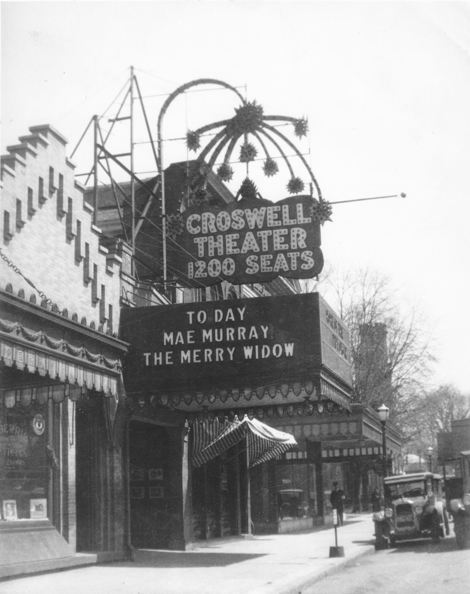 The Croswell Theater marquee displays showtimes and a message, with a decorative sign above and a street scene with cars and buildings.