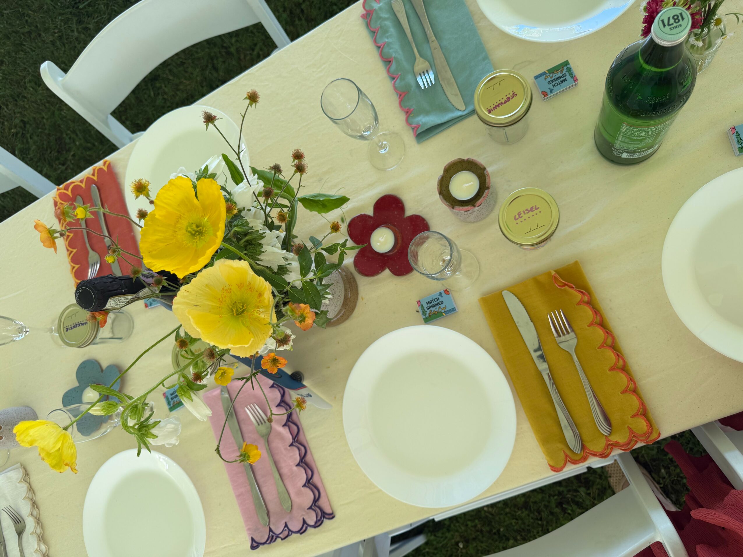 Table setting with plates, cutlery, a floral centerpiece, drinks, and colorful napkins, viewed from above.