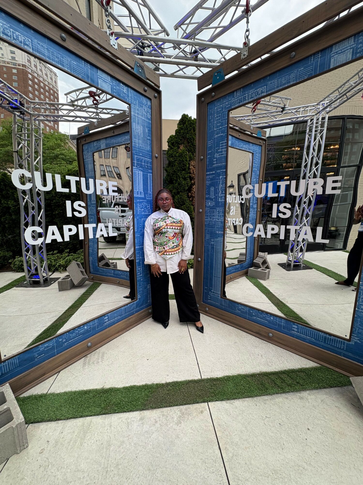 Person standing in front of large blue display panels with text about culture and capitalism, outdoors on sidewalk.