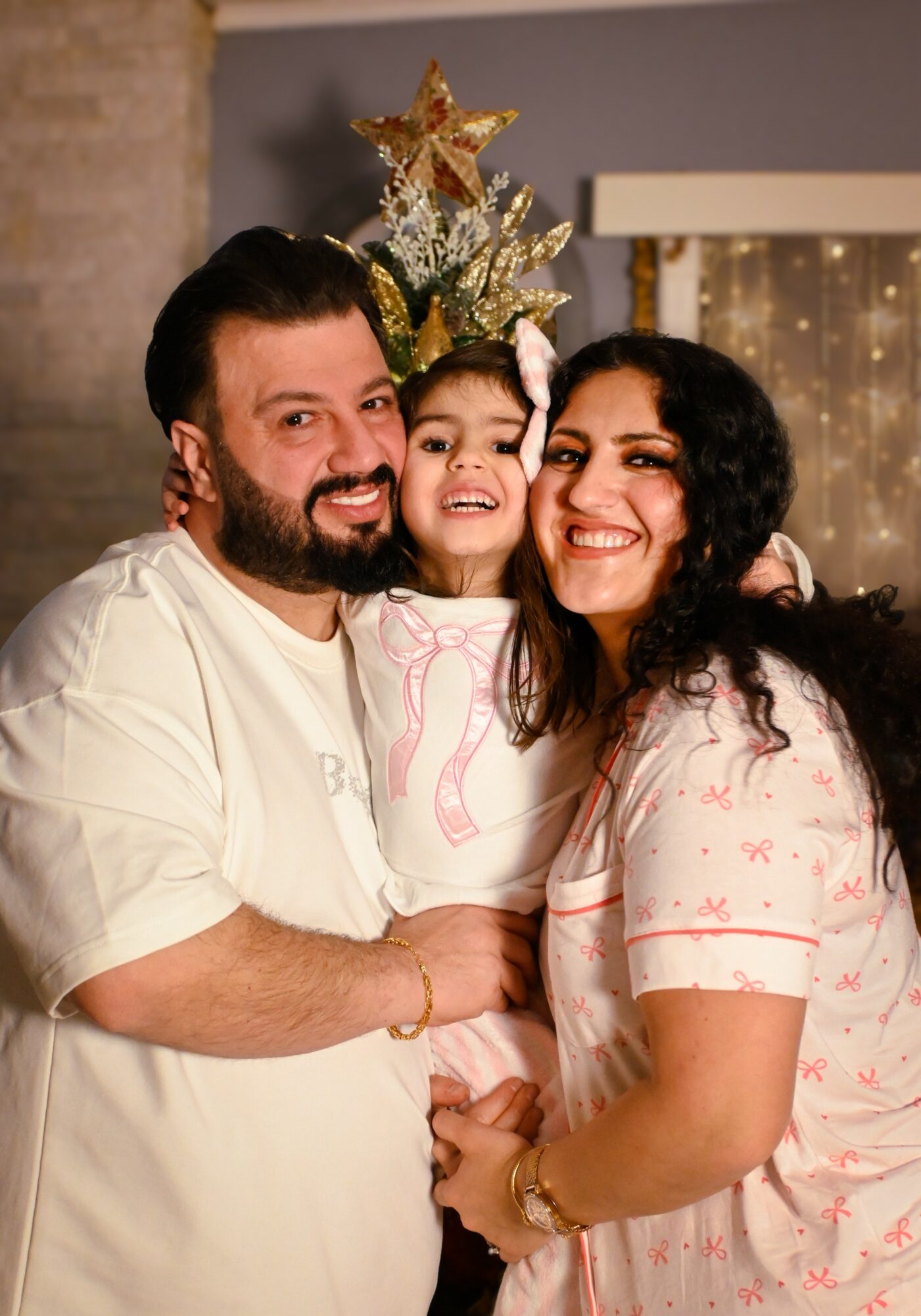 Three people smiling, standing close, with a decorated Christmas tree in the background.