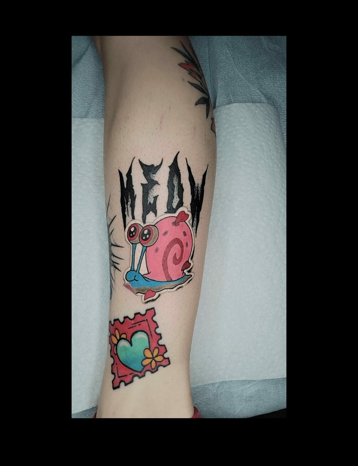 Tattoo of a pink snail with a blue eye on a person's arm, with colorful heart and abstract designs nearby.