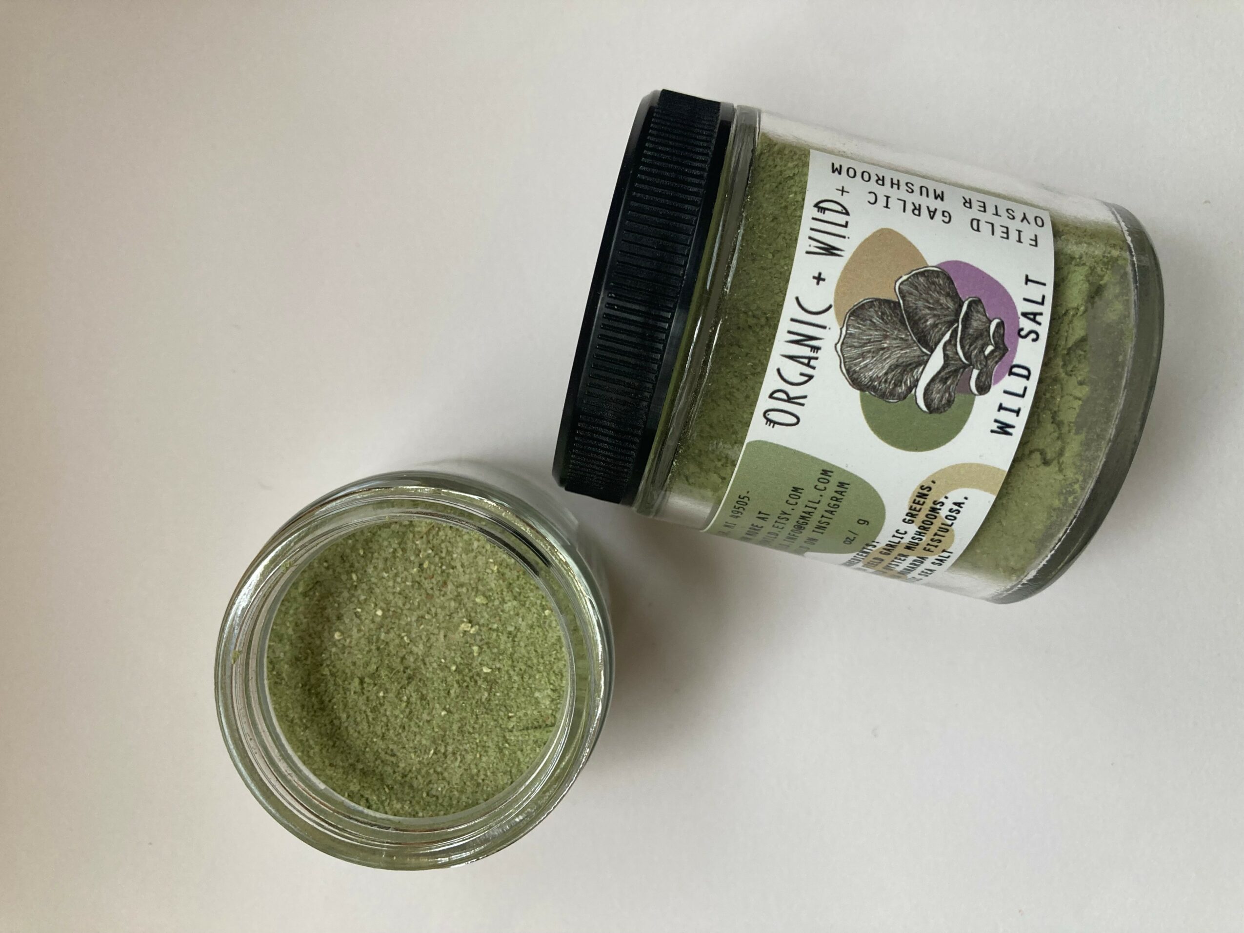 Open jar of green organic matcha powder with lid nearby on white surface.