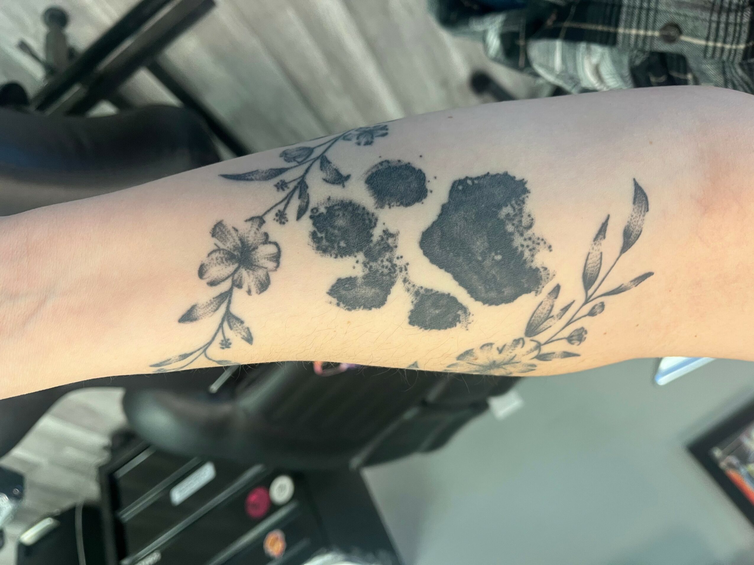 Tattoo of inkblot-like shapes surrounded by floral designs on person's forearm.