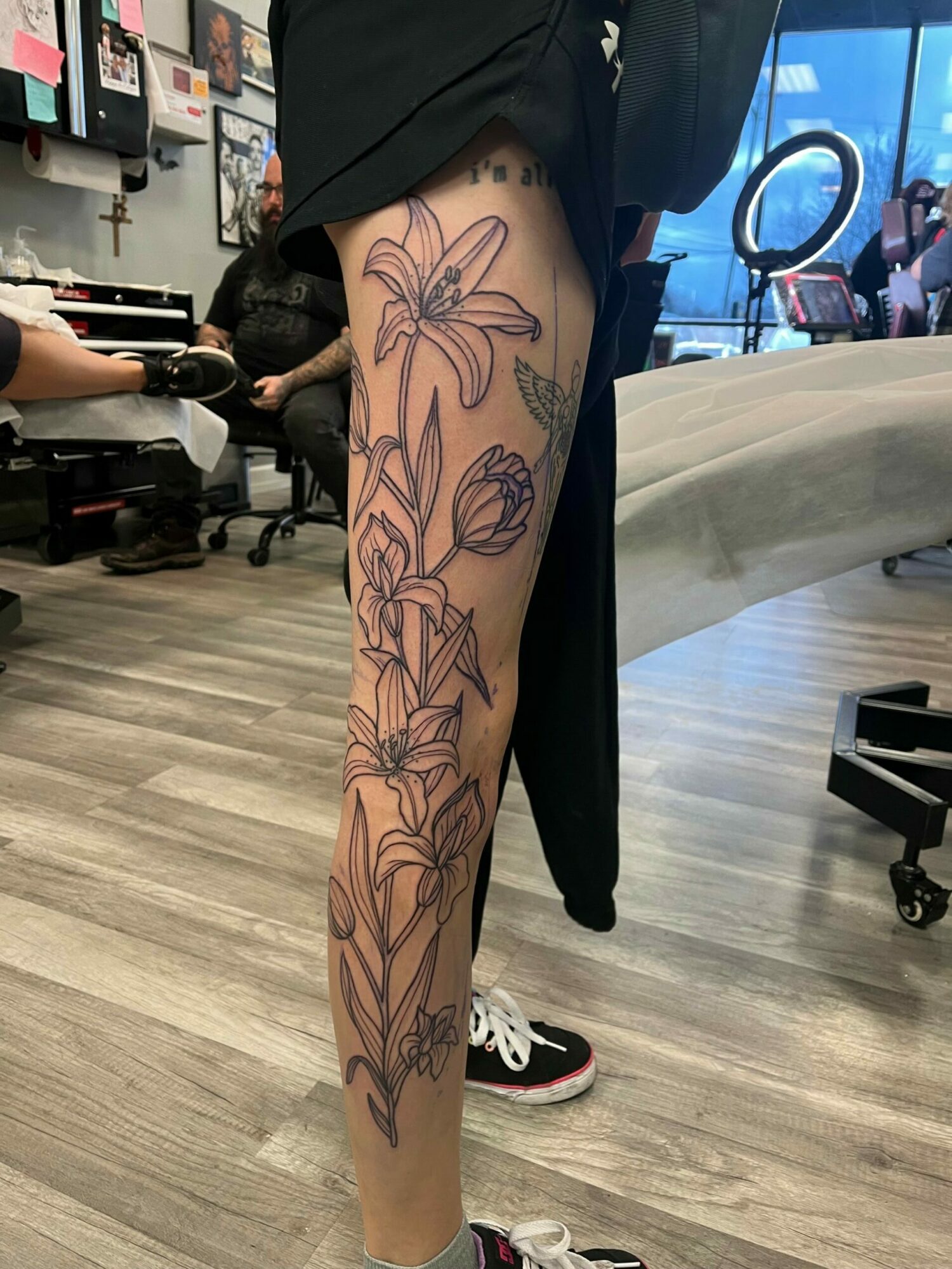 Person with a large floral tattoo on their leg, sitting in a room with a curved white sofa and wooden floor.