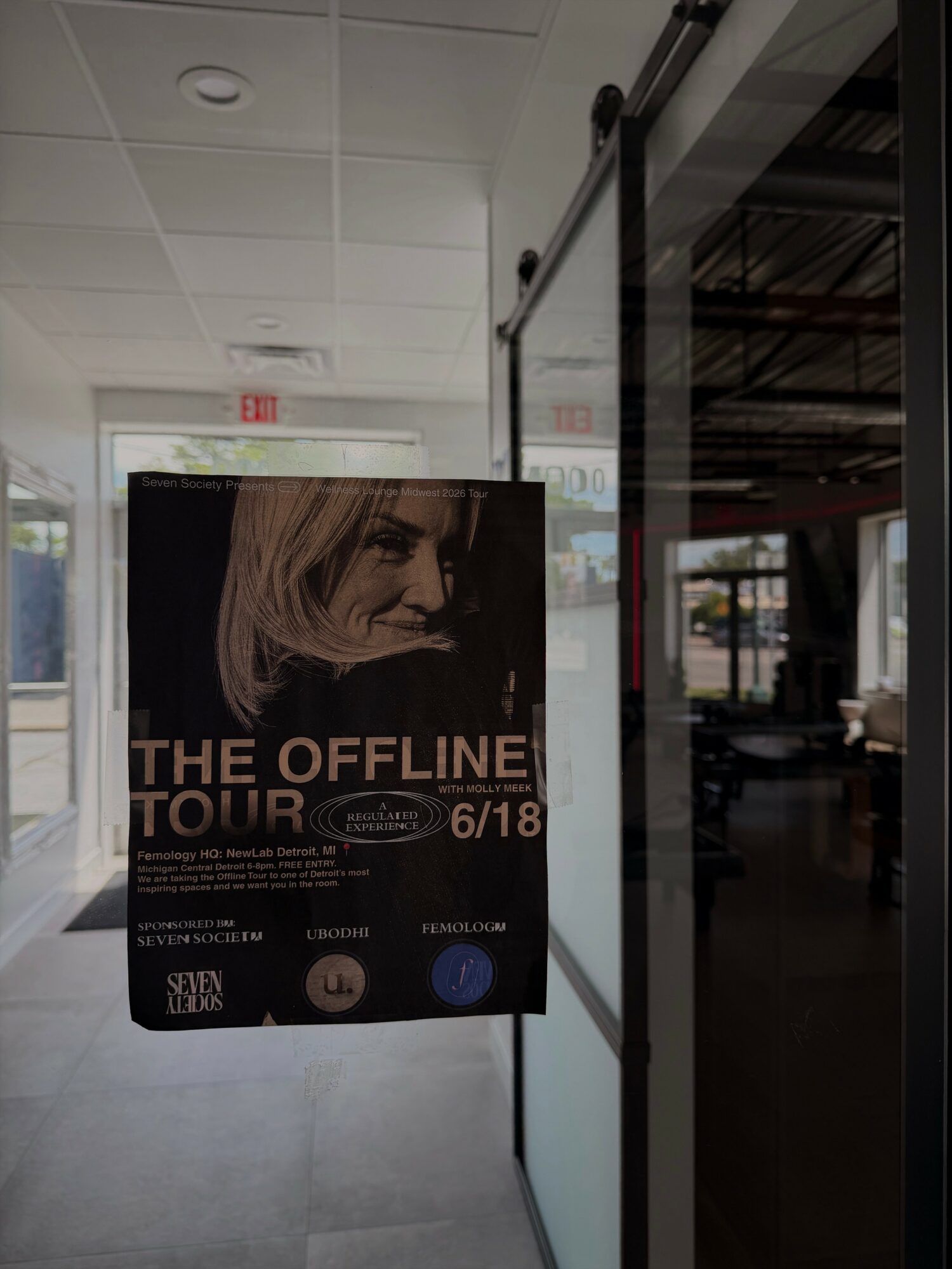 Poster advertising The Offline Tour with a woman's face, event date, and venue details, inside a building with glass doors.