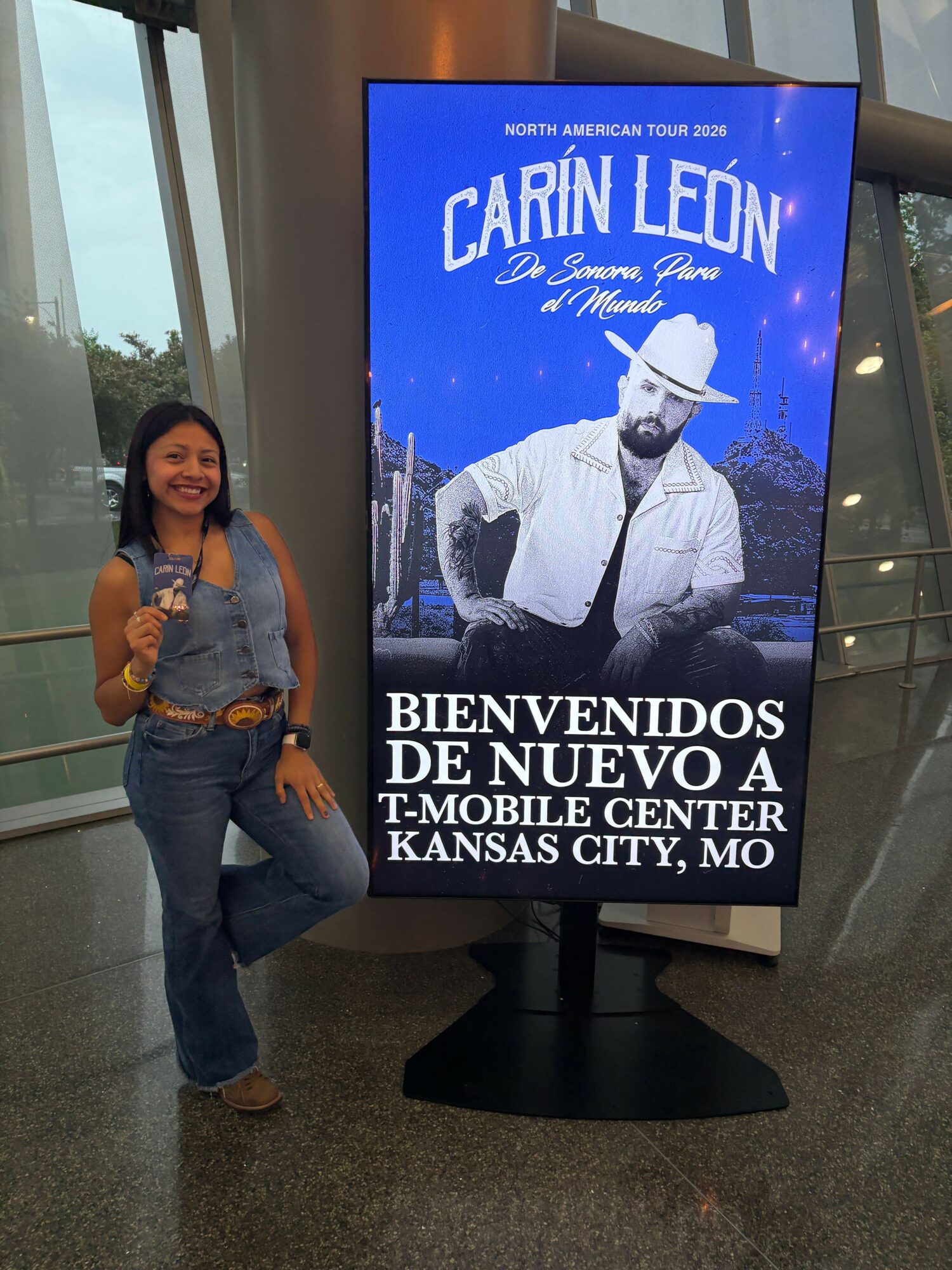 Woman standing next to a digital display with a book cover featuring a man in a hat and text in Spanish.