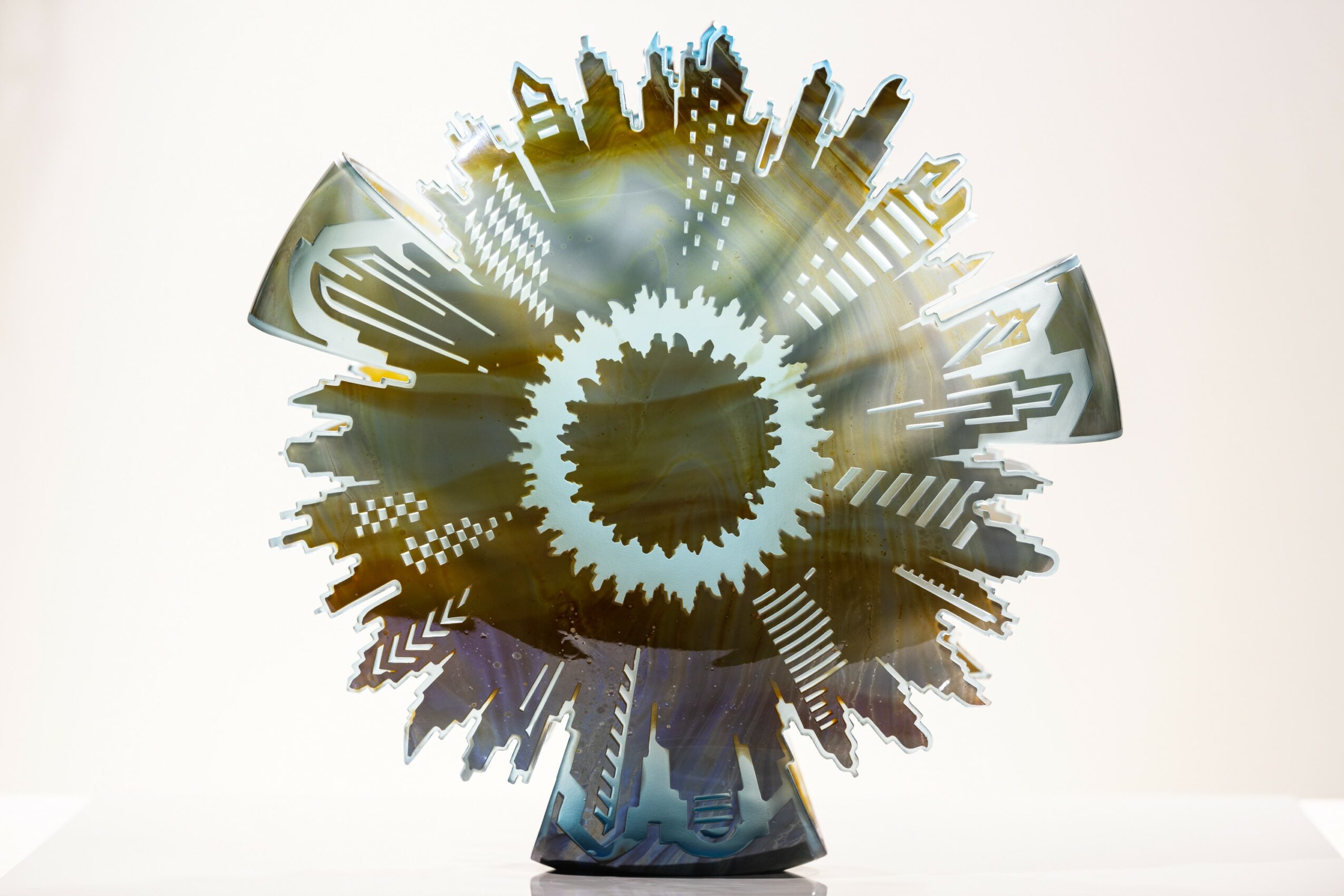Abstract metallic sculpture with gear-like center and radiating arrow shapes, reflective surface, on a white background.