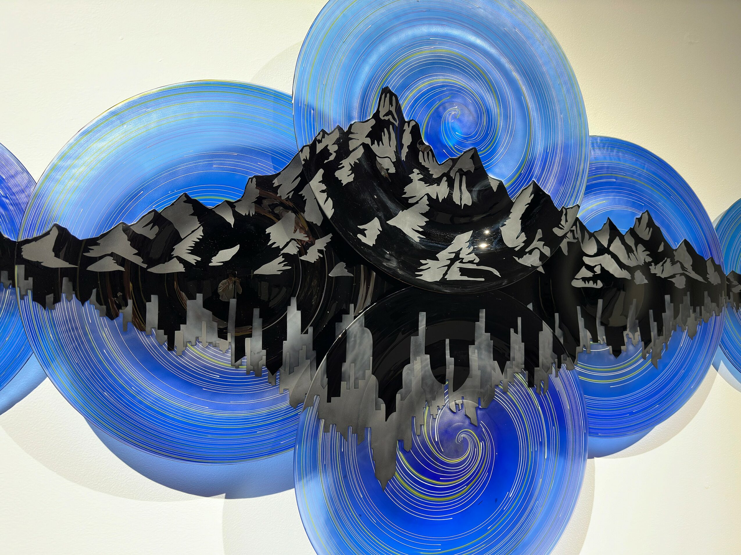 Abstract artwork of a mountain range reflected in water, surrounded by blue circular patterns, on a light background.