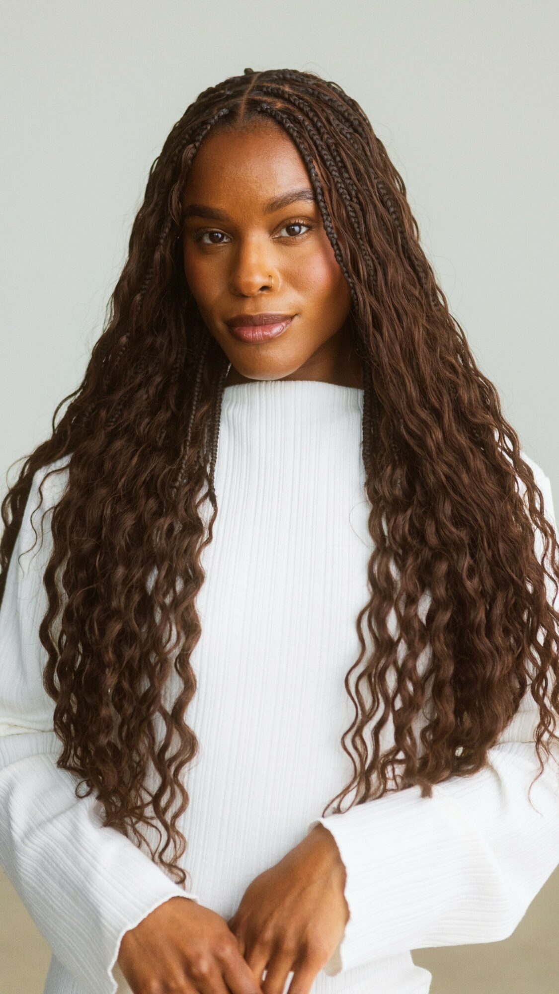 Woman with long, curly hair wearing a white sweater, looking at the camera, neutral background.