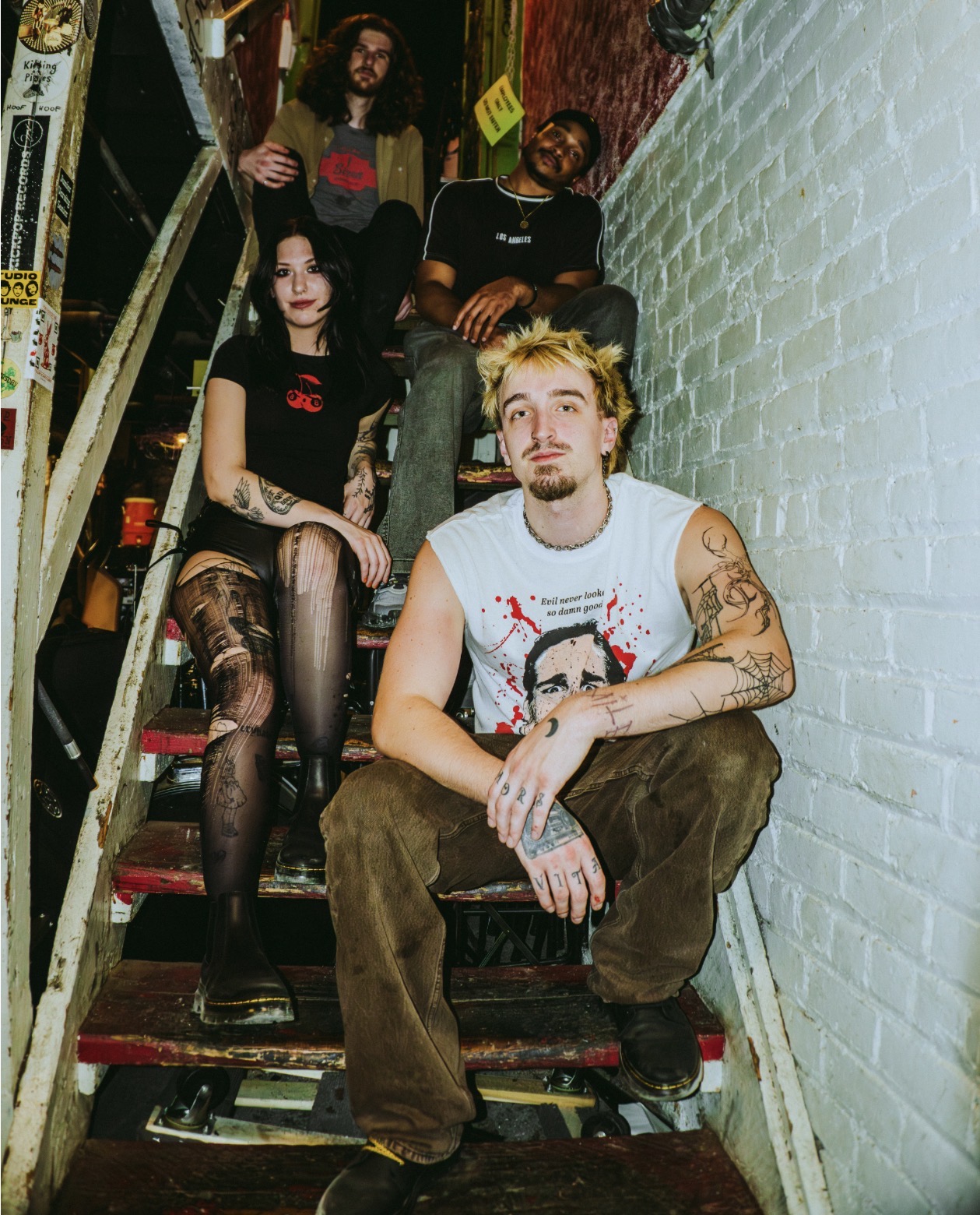 Group of five people sitting on a staircase with a brick wall on the right side, posing for a photo.