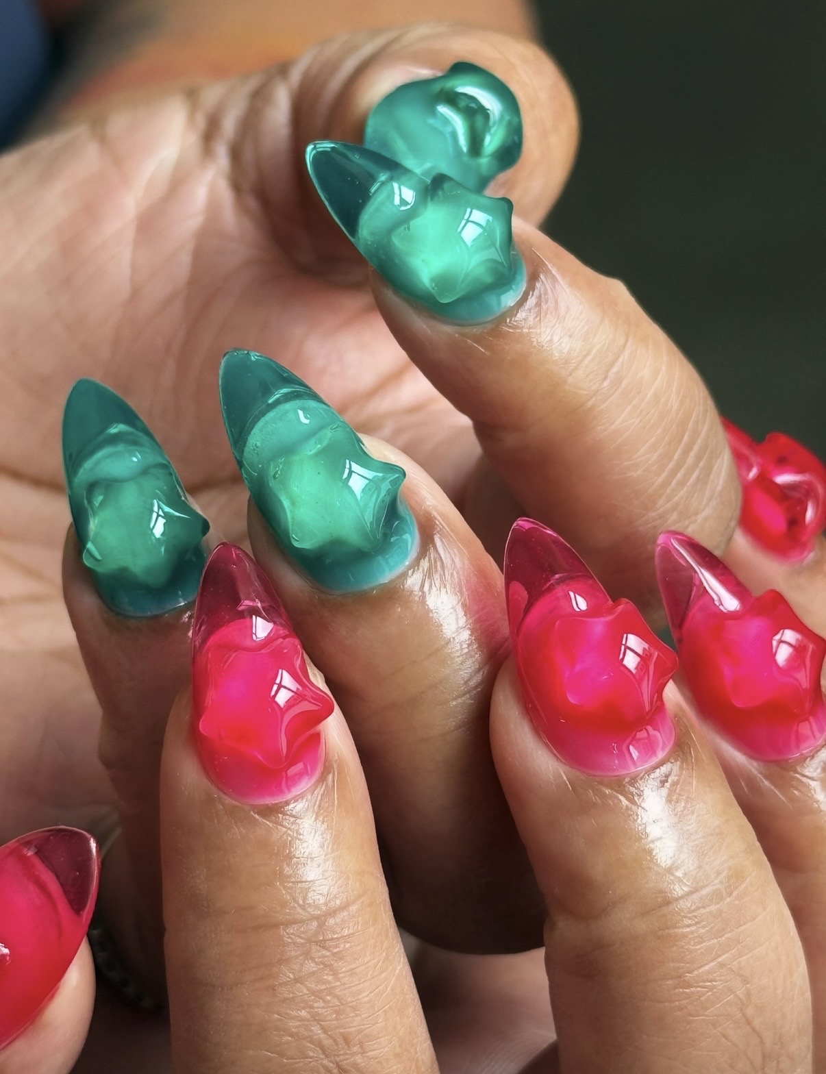 Close-up of fingers with colorful, glossy, nail art in green and pink, shaped like small cones or peaks.