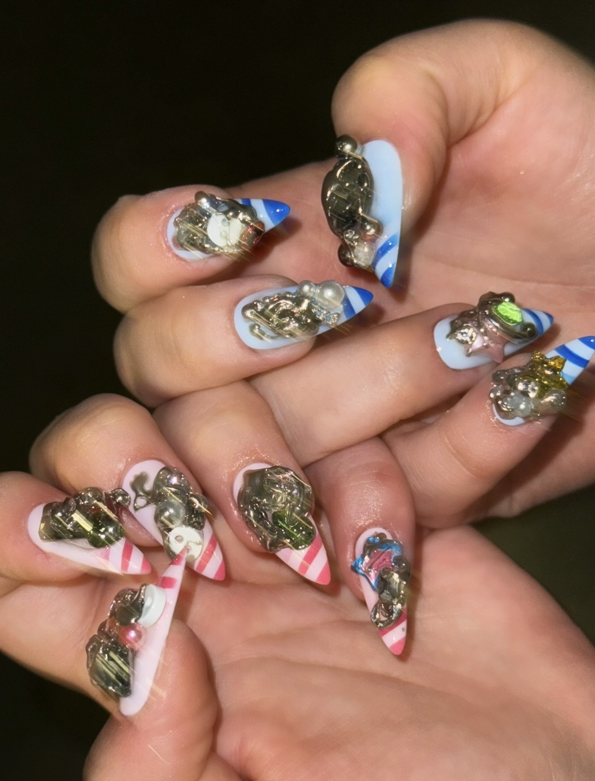 Close-up of hands with decorated nails featuring various colors, patterns, and embellishments.