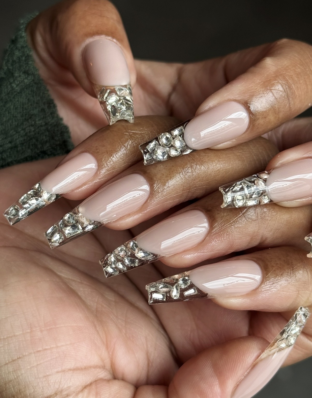 Close-up of hands with long, decorated nails and rhinestone embellishments, intertwined with another person's hand, dark background.