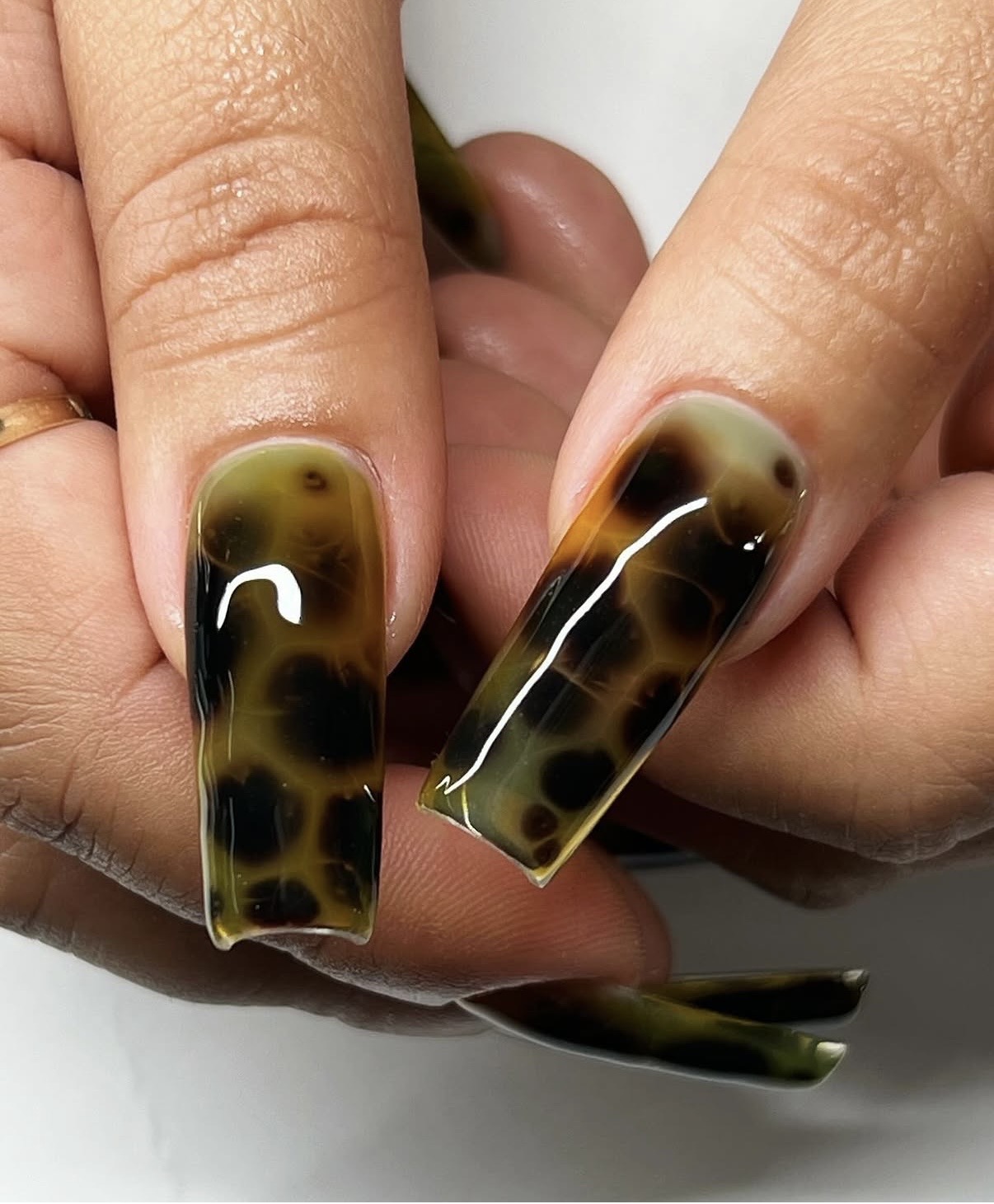 Close-up of two hands with long, rectangular, tortoiseshell-patterned acrylic nails, showing detailed nail design and skin texture.
