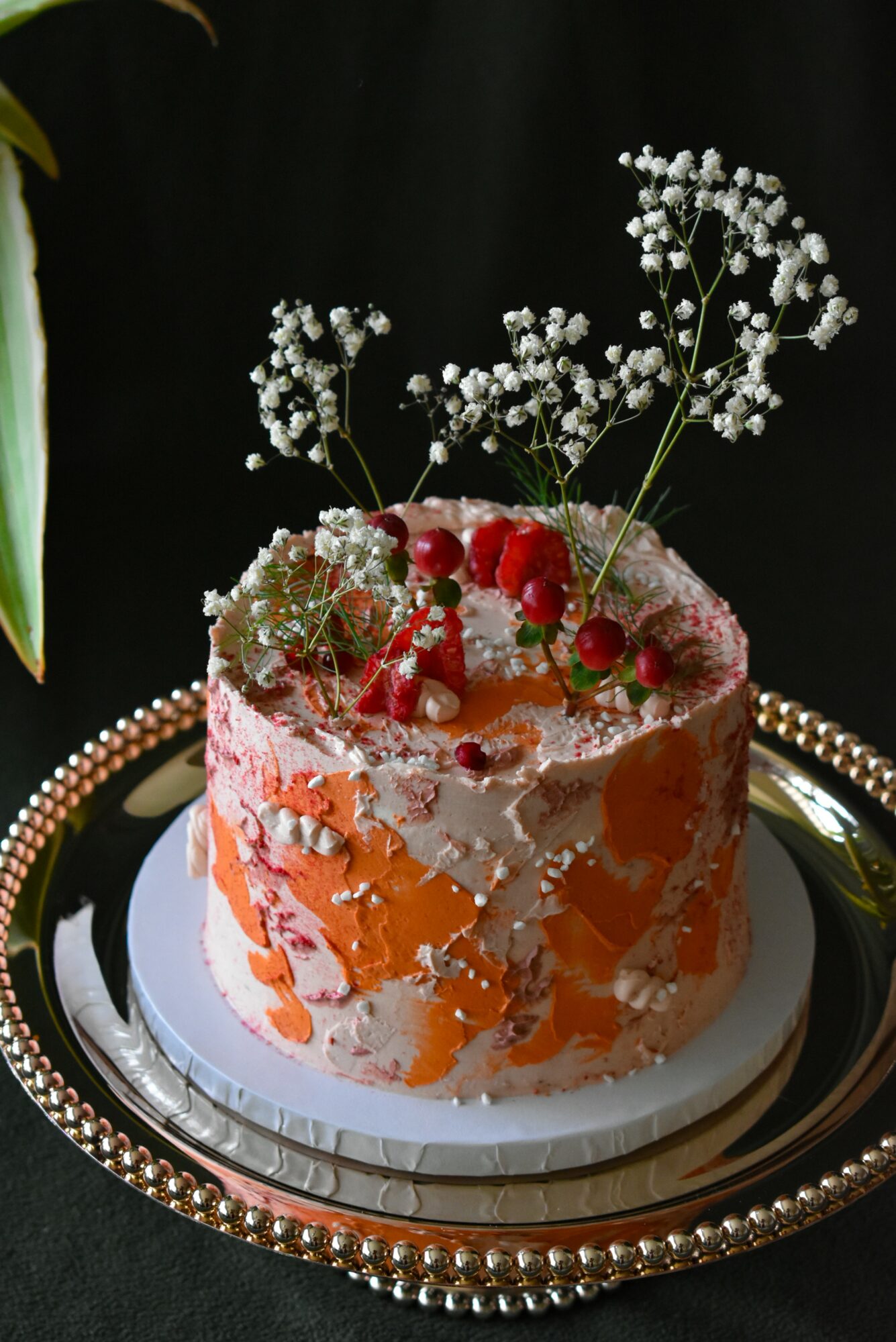 Decorative cake with white and orange icing, topped with red berries and white flowers, on a black background.