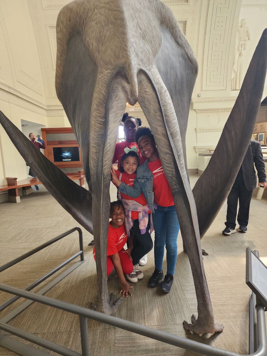 People inside a large dinosaur skeleton exhibit, with some children and adults, in a museum setting.