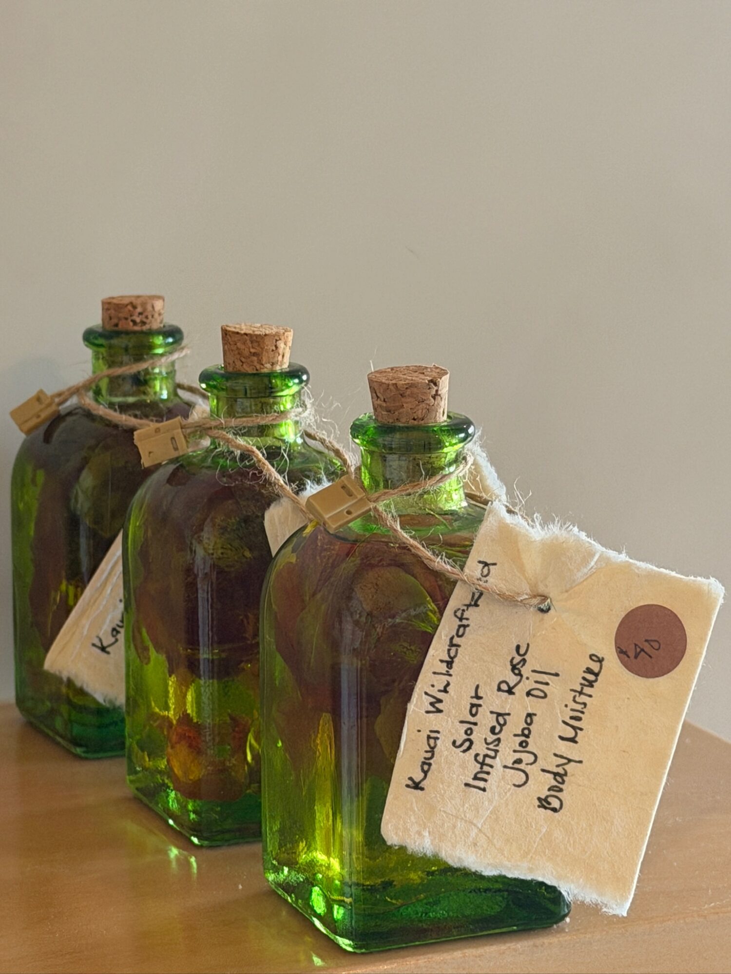 Four small green glass bottles with cork stoppers and tags, placed on a wooden surface against a plain background.