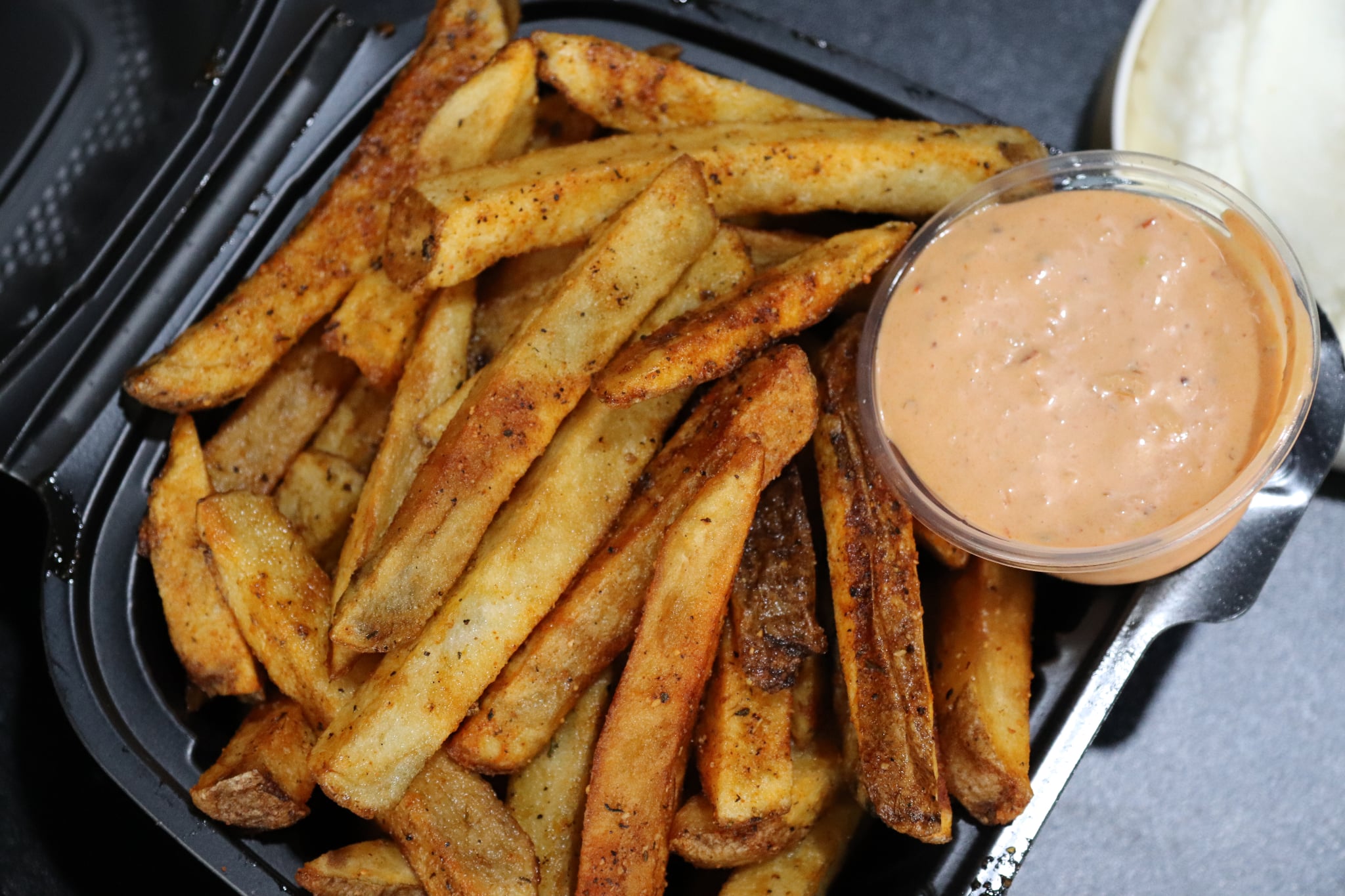 French fries with a side of dipping sauce in a small glass bowl, served in a black container.
