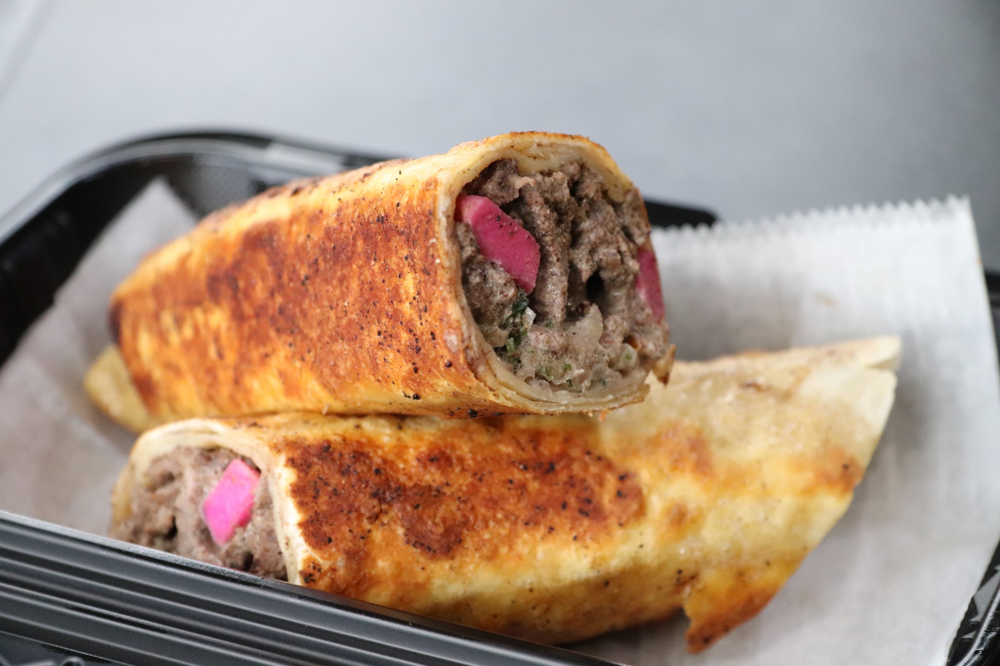 Two fried spring rolls with meat filling and pink pickled vegetables inside, placed on a paper-lined tray.