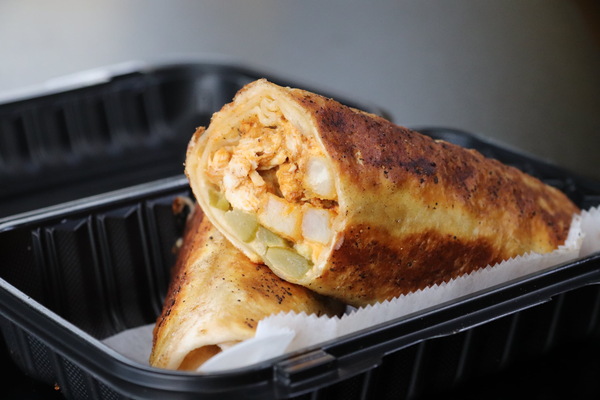 Two toasted sandwiches in a black plastic container, one partially inside the other, with a golden-brown crust and filling visible.