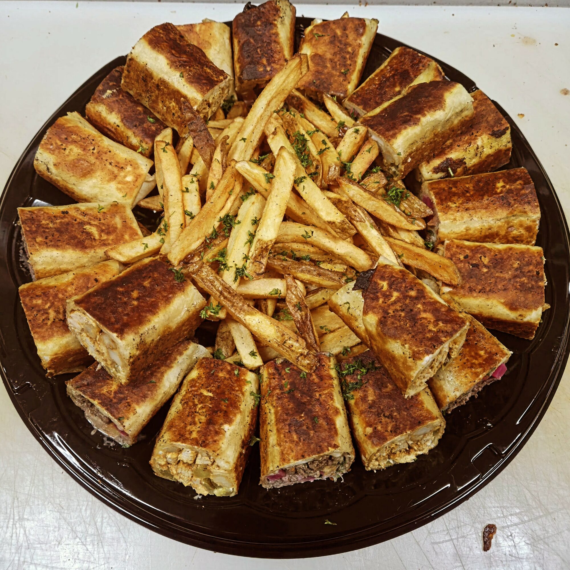 Plate with fried sandwiches and French fries arranged in a circle on a black plate.