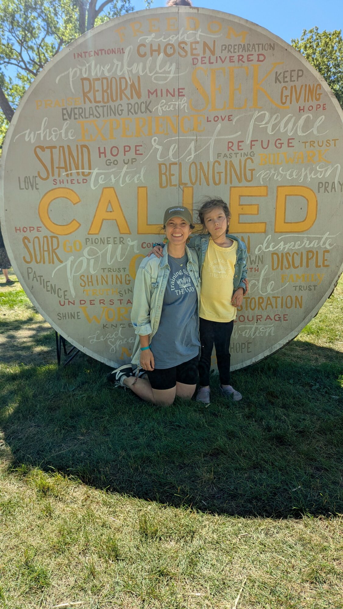 Two children standing in front of a large circular mural with words like 'called,' 'belonging,' and 'hope.'