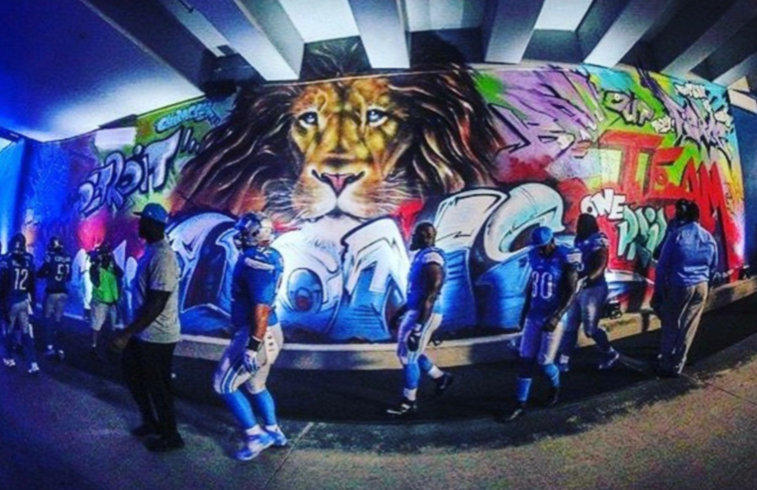 Group of people in front of a colorful graffiti mural featuring a lion's face, with vibrant designs and text.