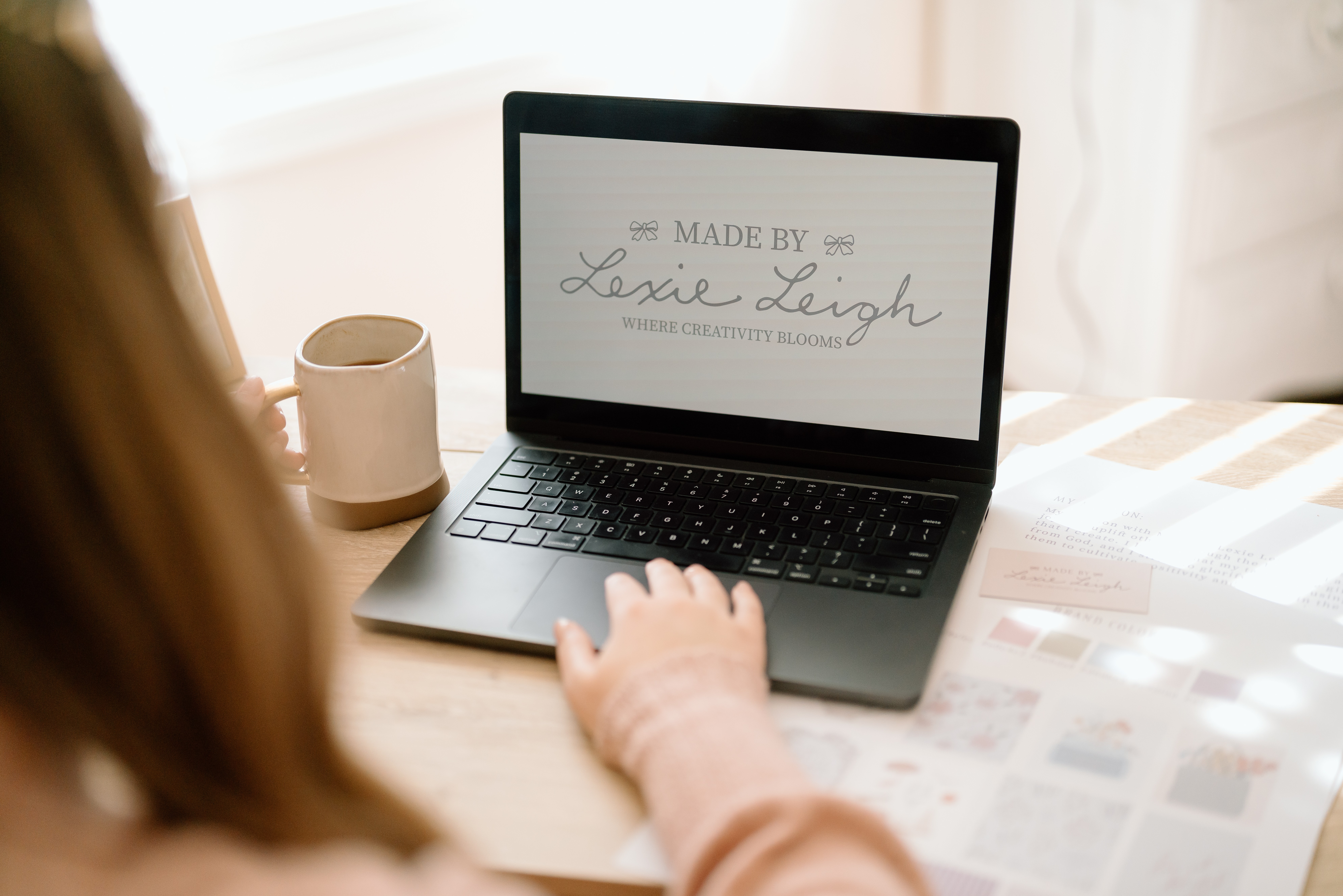 Person using a laptop on a table with a mug nearby, screen displaying text, in a bright room.