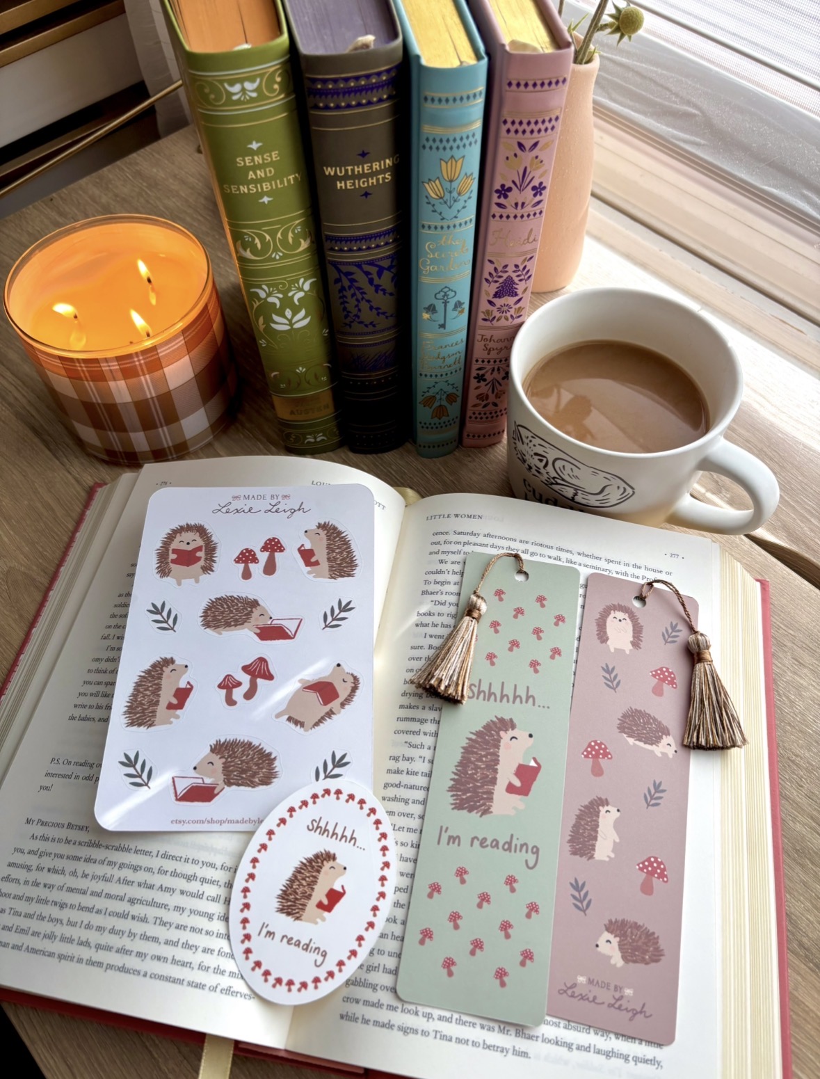 Open book with bookmarks, a cup of coffee, a lit candle, and colorful books on a windowsill, with a cozy atmosphere.