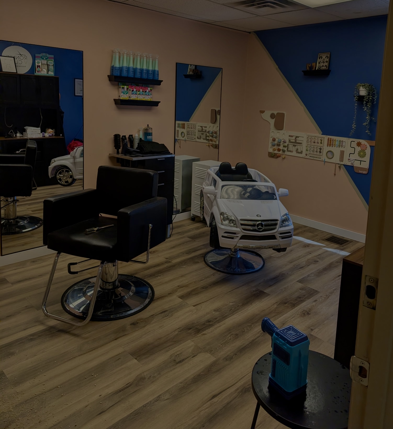 Salon with styling chair, mirror, and toy car for children, colorful wall decor, and wooden flooring.