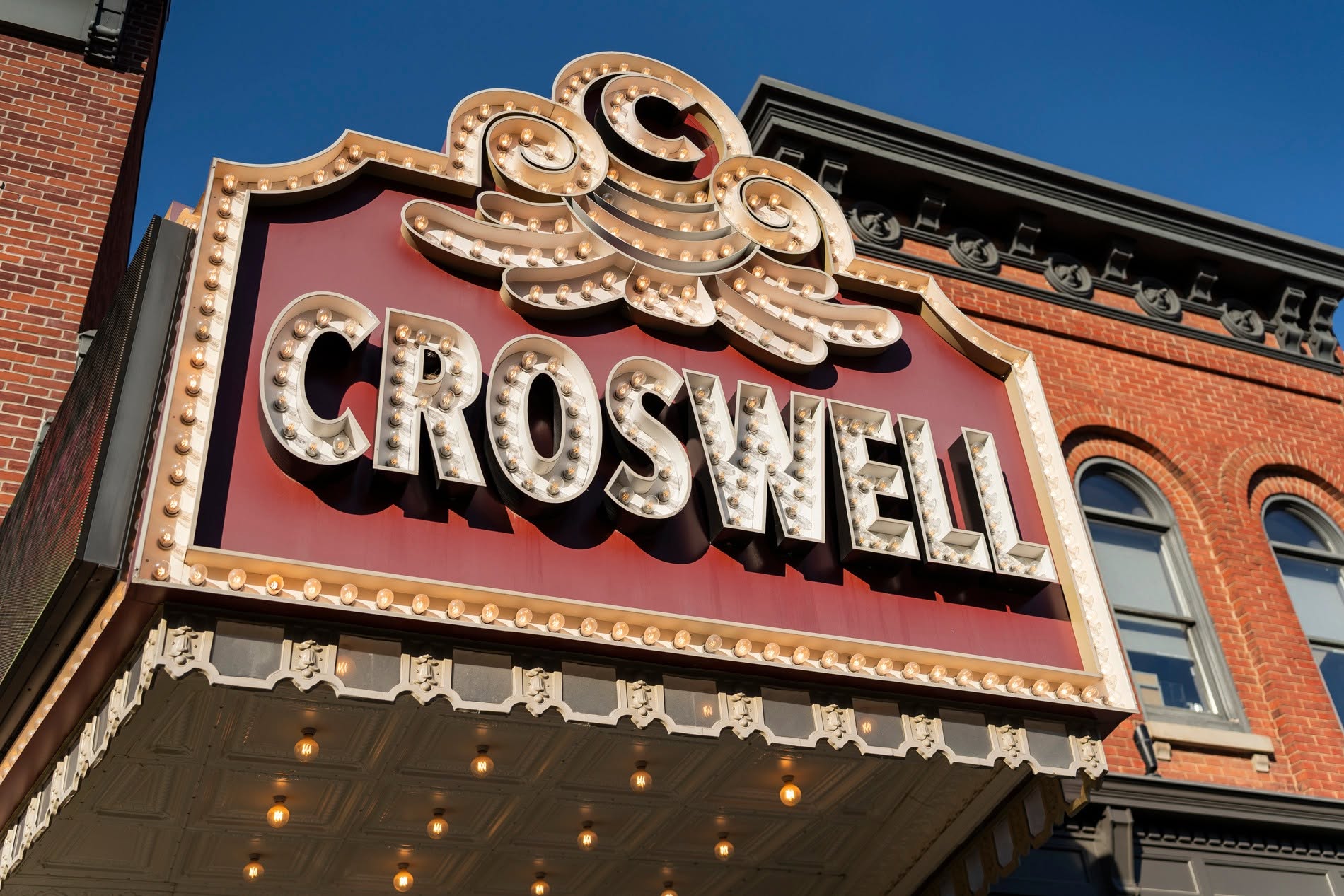 Marquee sign with the word 'CROSWELL' in large letters, decorative elements, and a pink background, attached to a brick building.