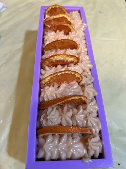 Long purple container filled with pink frosting and orange slices on top, placed on a light-colored surface.