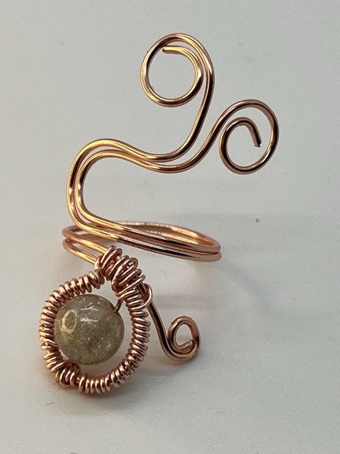 Wire sculpture with a spiral design and a round stone at the base, on a plain background.
